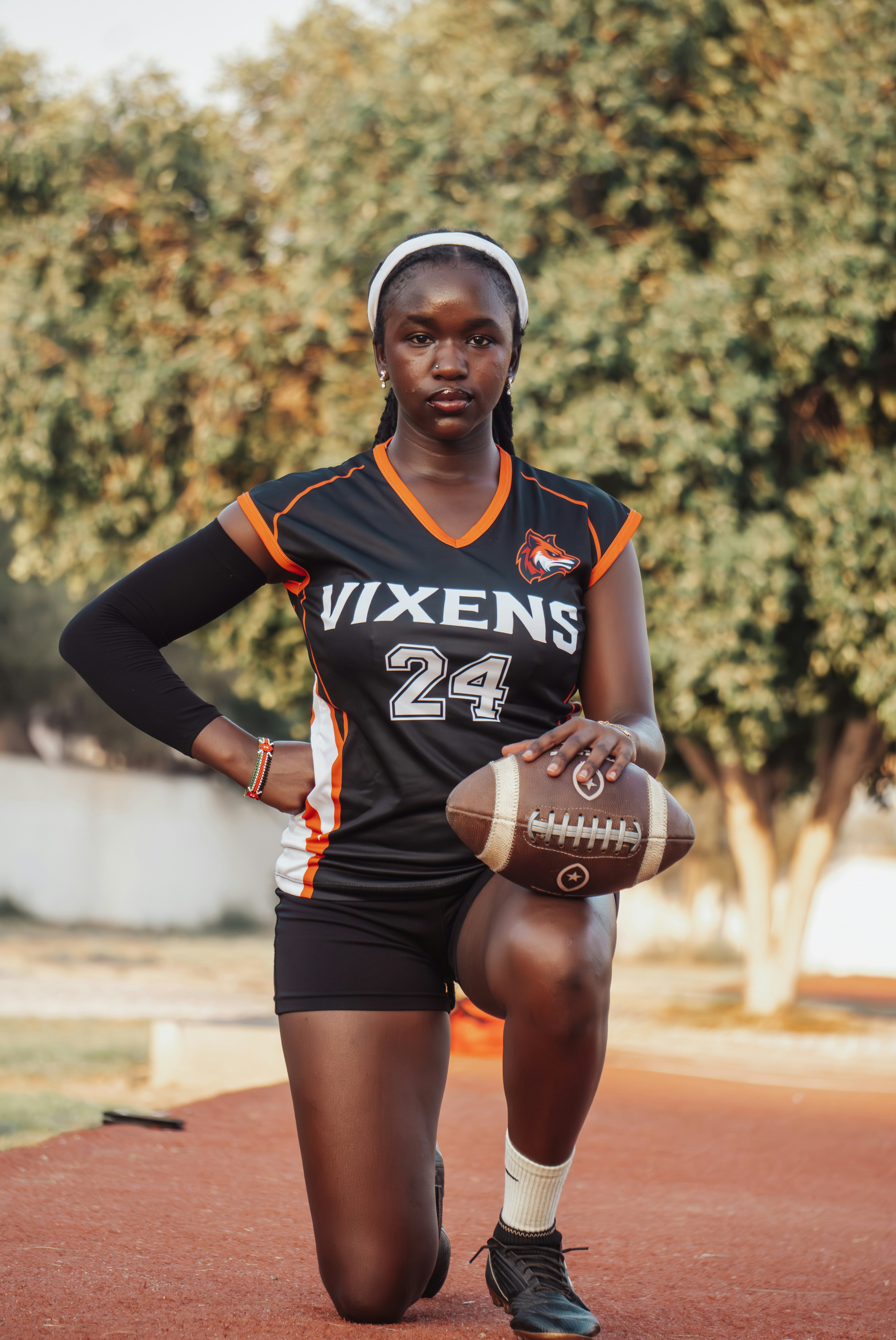 Uma mulher com uma camisa preta e laranja ajoelhada com uma bola de futebol americano