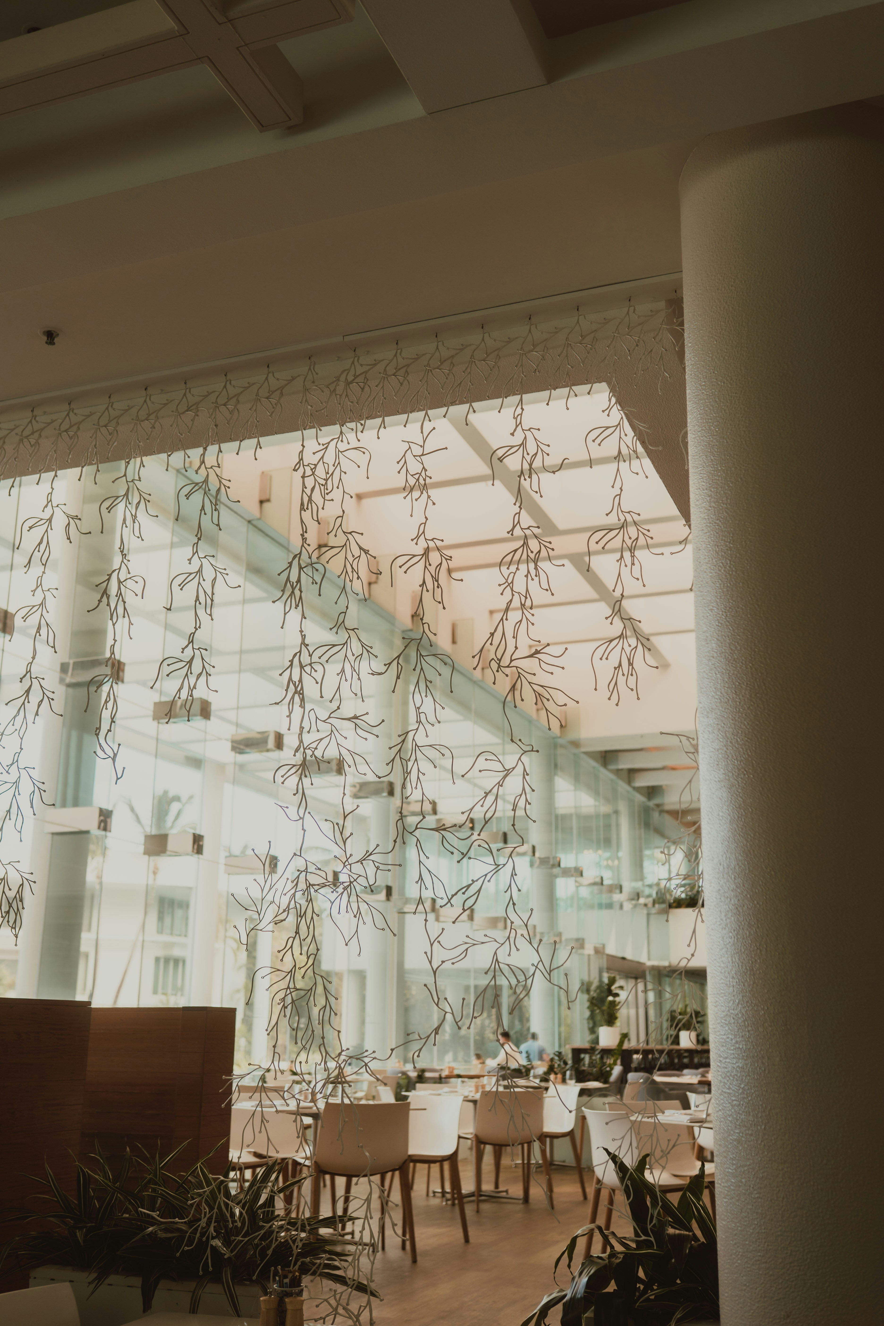 White decorative hanging branches in a bright restaurant with glass walls and tables