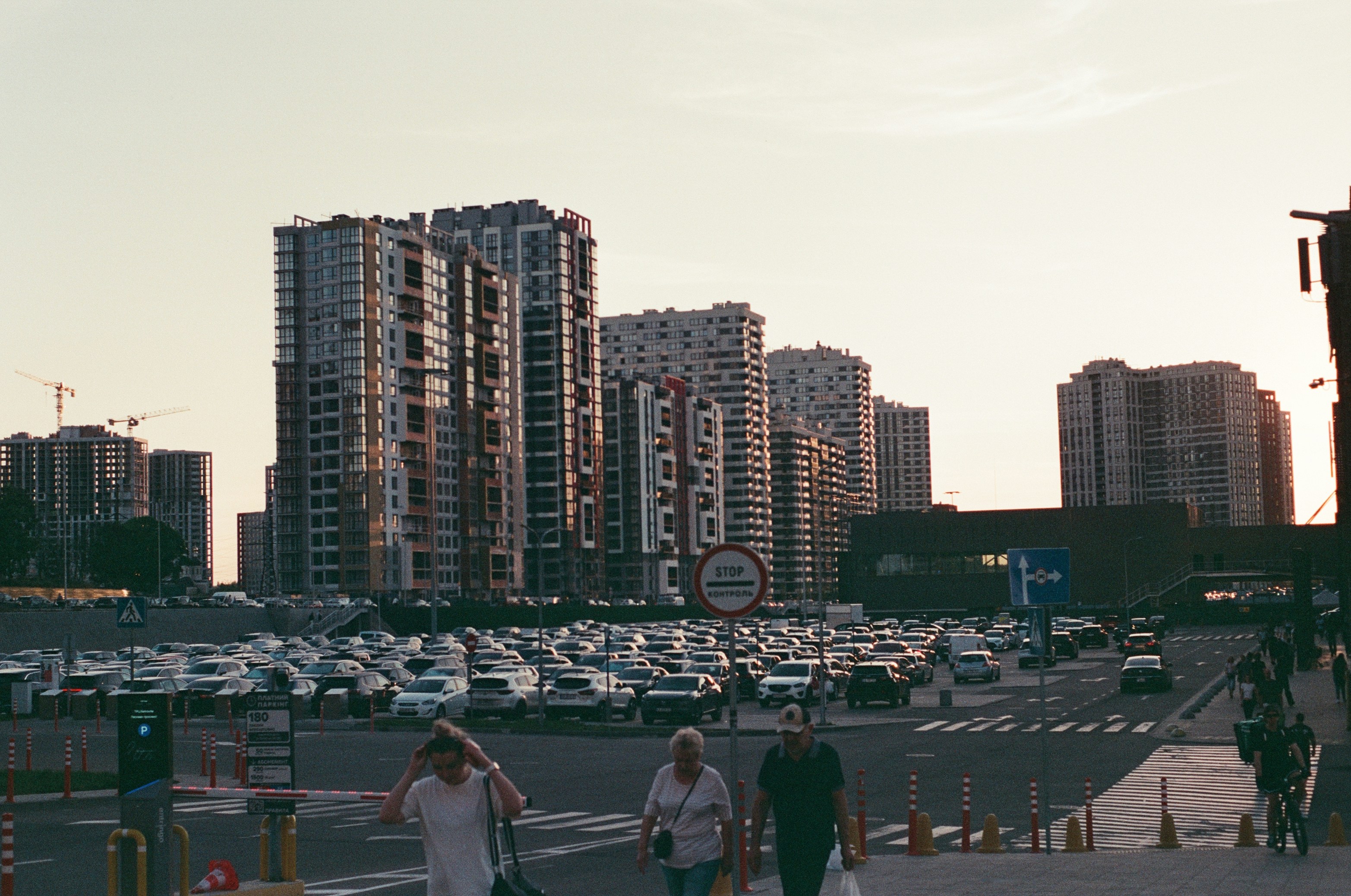 People walking across a parking lot in front of tall apartment buildings at dusk