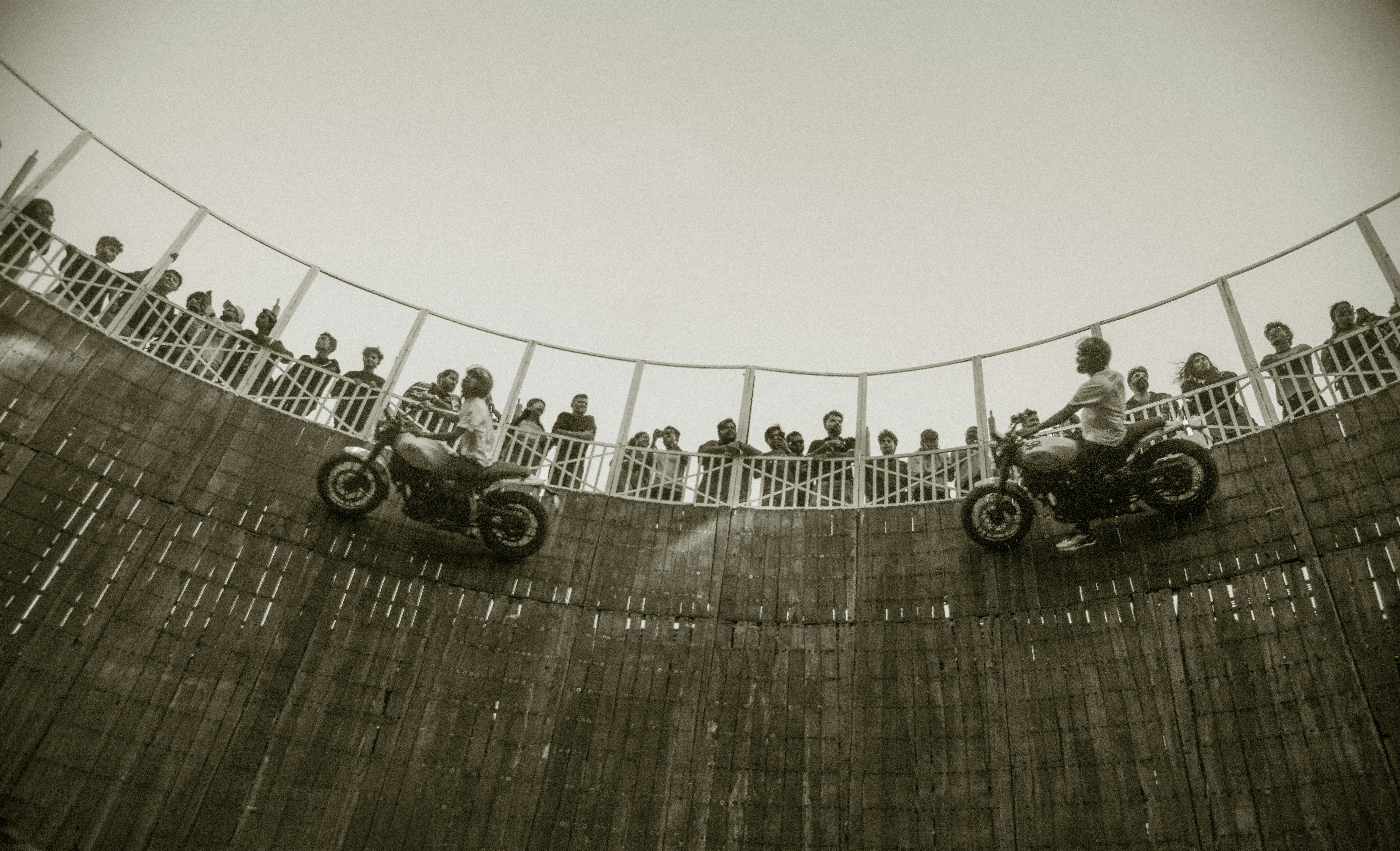 Two motorcyclists riding on the vertical wooden walls of a well of death