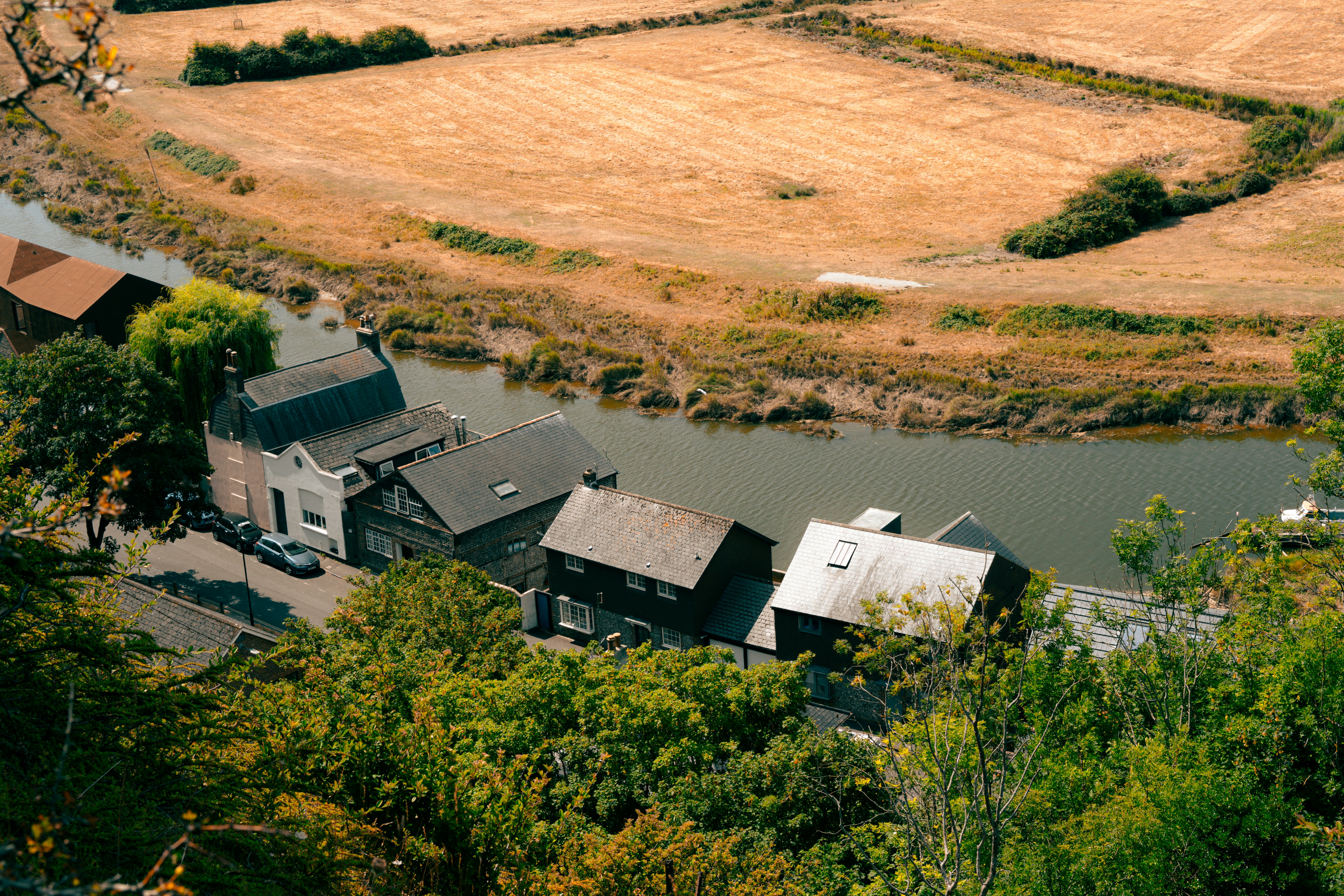 A row of houses along a river beside a dry golden field