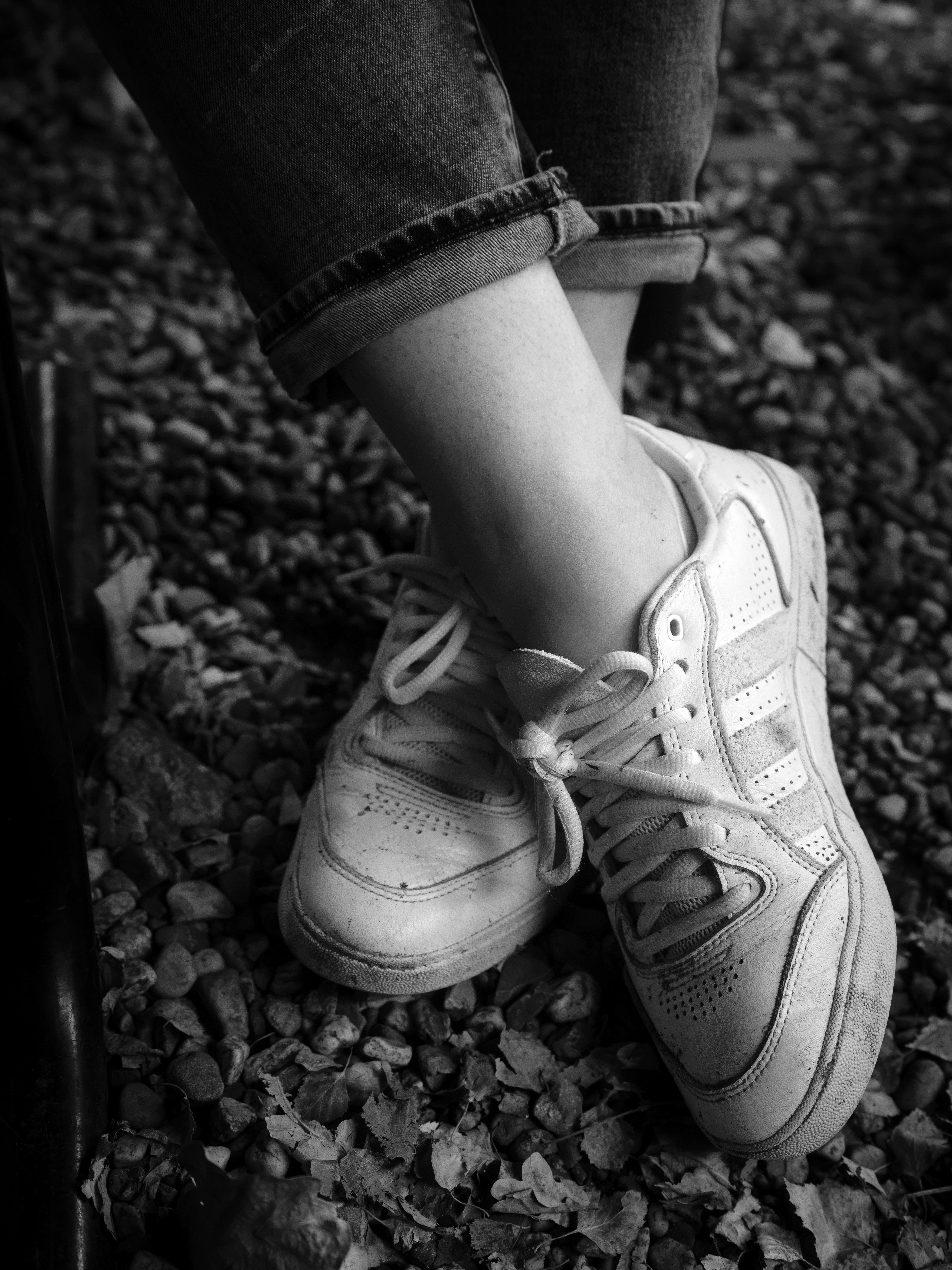 A person wearing white sneakers and cuffed jeans standing on a gravel path