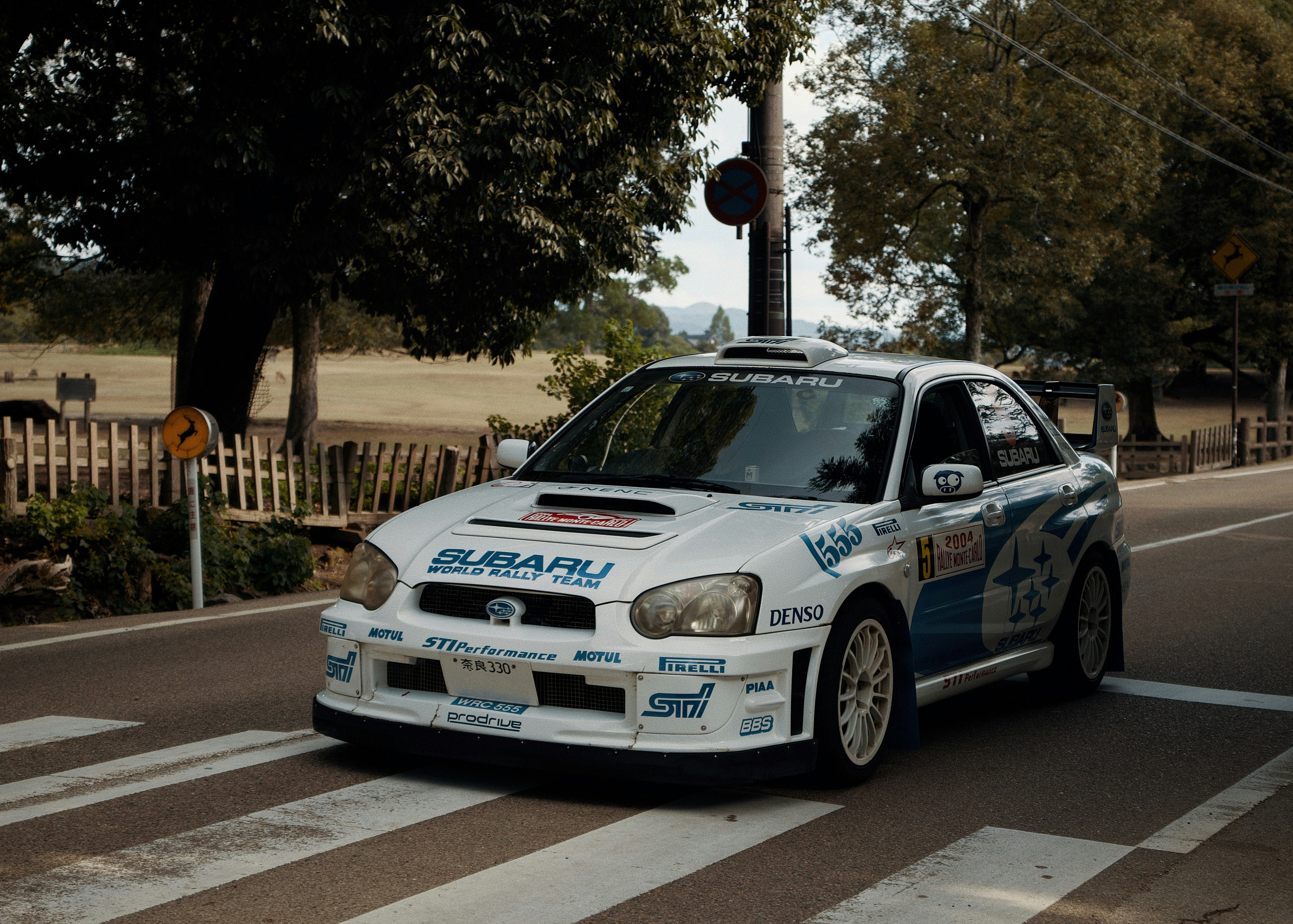 Ein weißes Rallyeauto fährt auf einer Straße in der Nähe eines Holzzauns und Bäumen