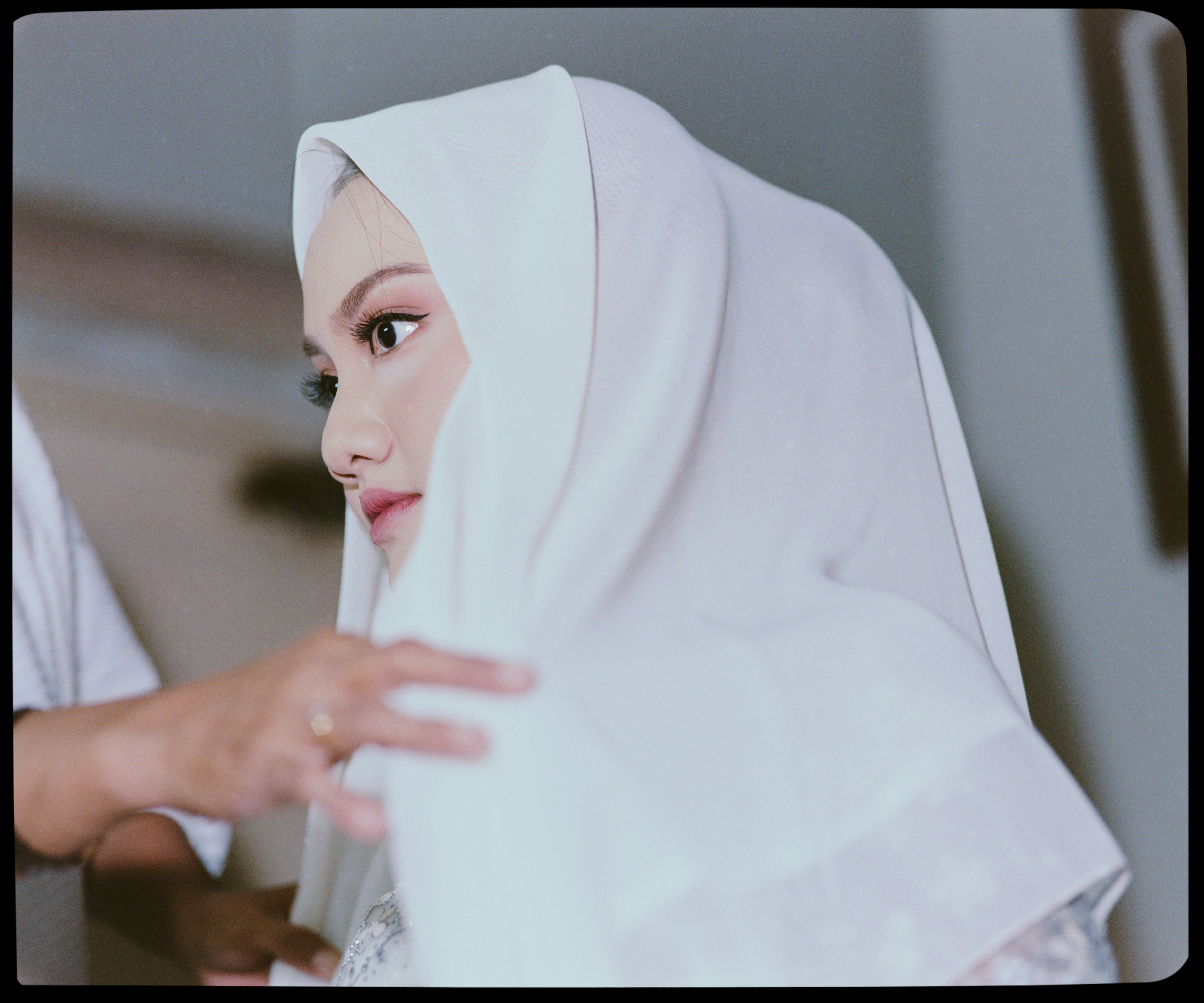 A person adjusting a white hijab on a woman with soft makeup
