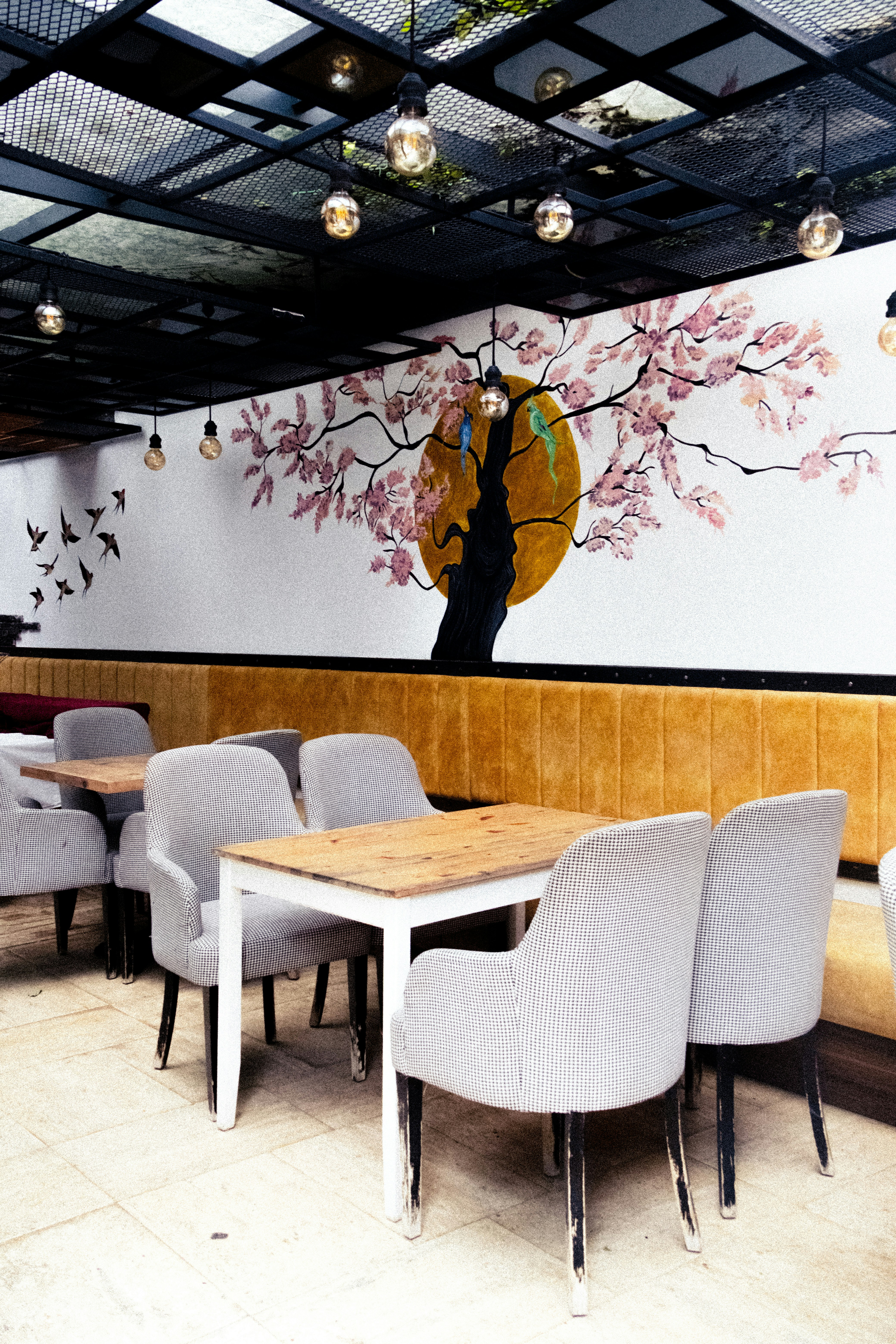 Des tables et des chaises dans un restaurant avec une fresque de fleurs de cerisier accrochée au mur