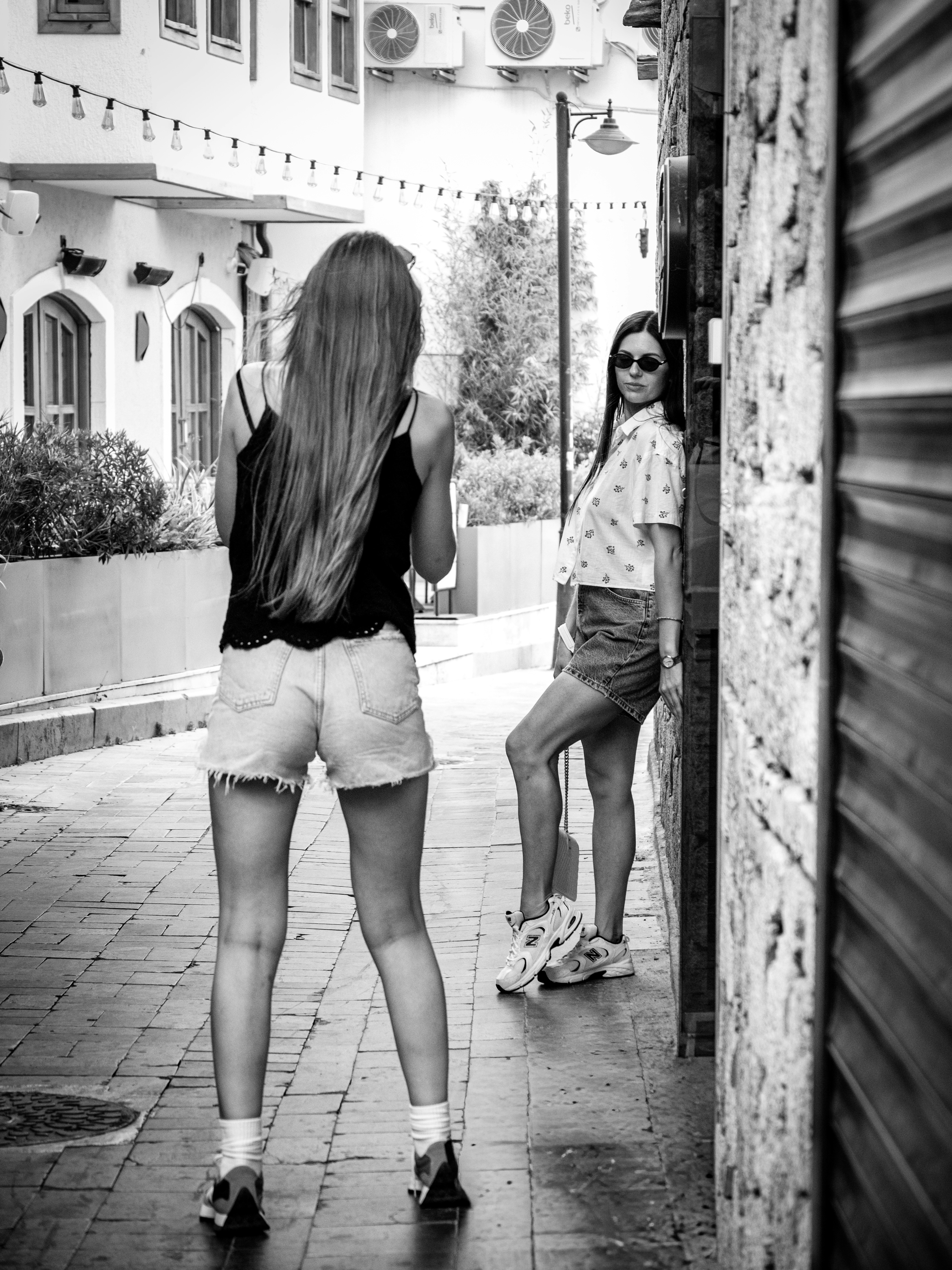 Une femme photographiant une autre femme adossée à un mur de pierre dans une ruelle étroite