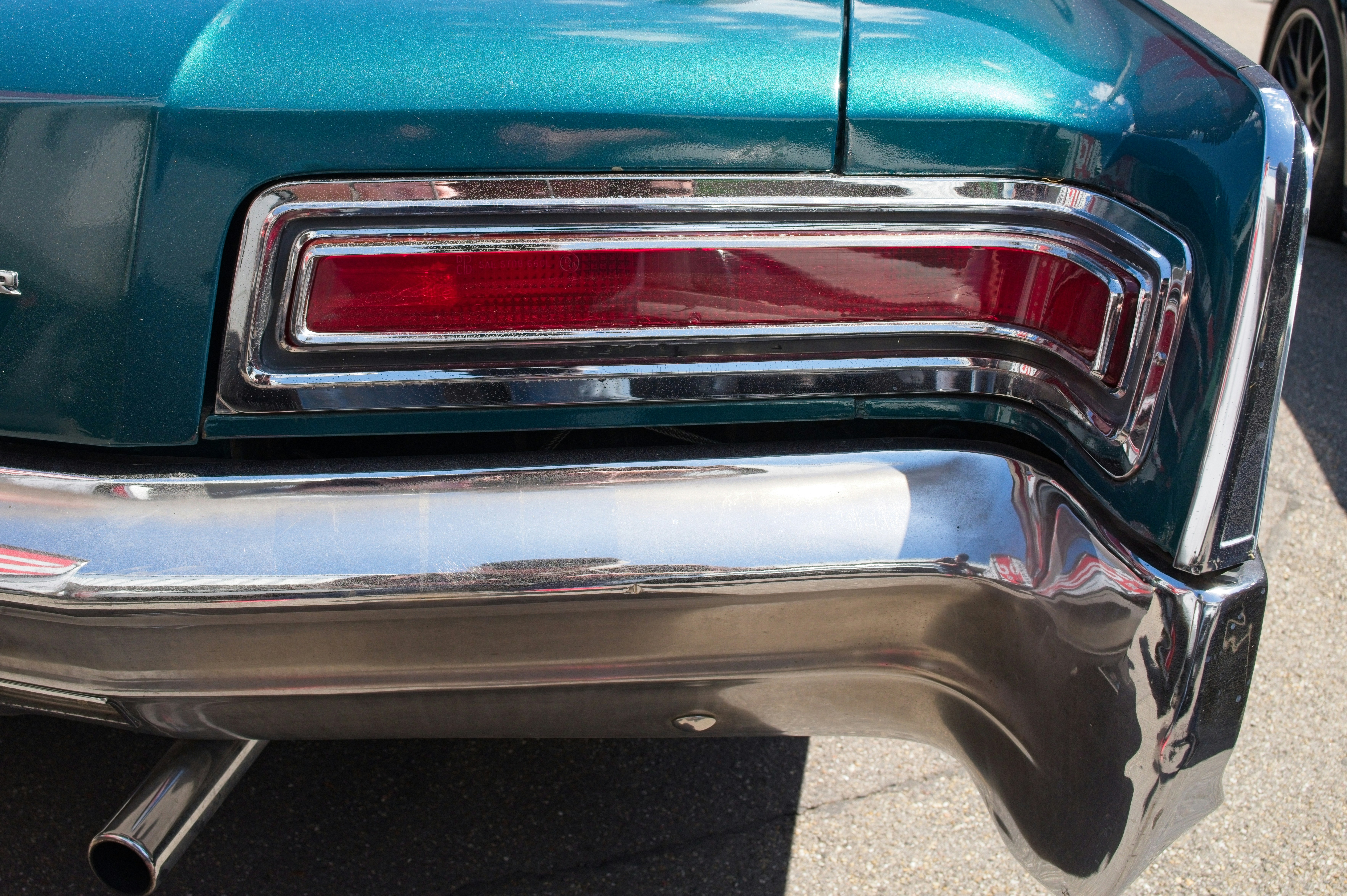The rear taillight and chrome bumper of a teal vintage car