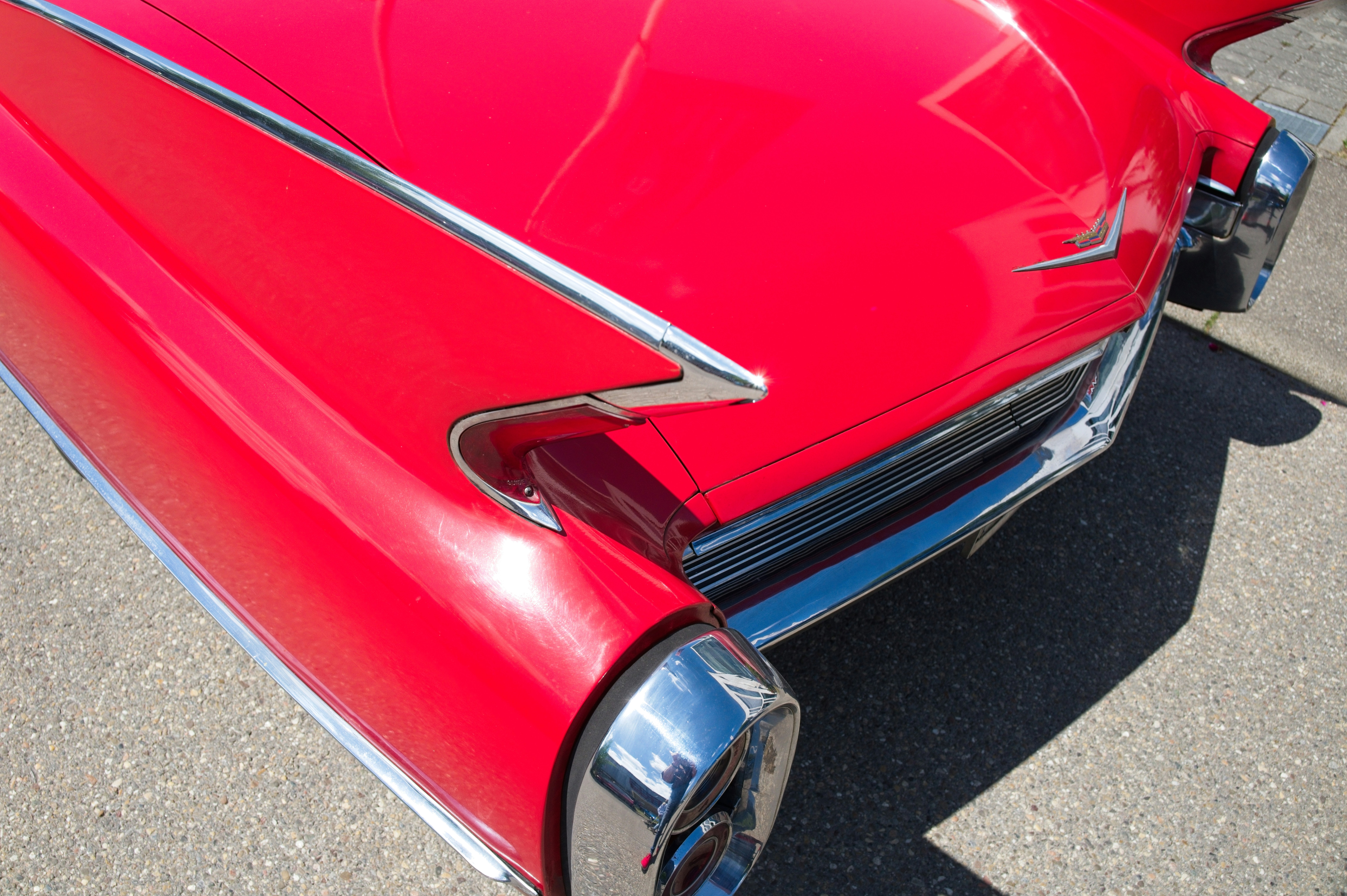 The rear tail fin and chrome taillight of a bright red vintage car