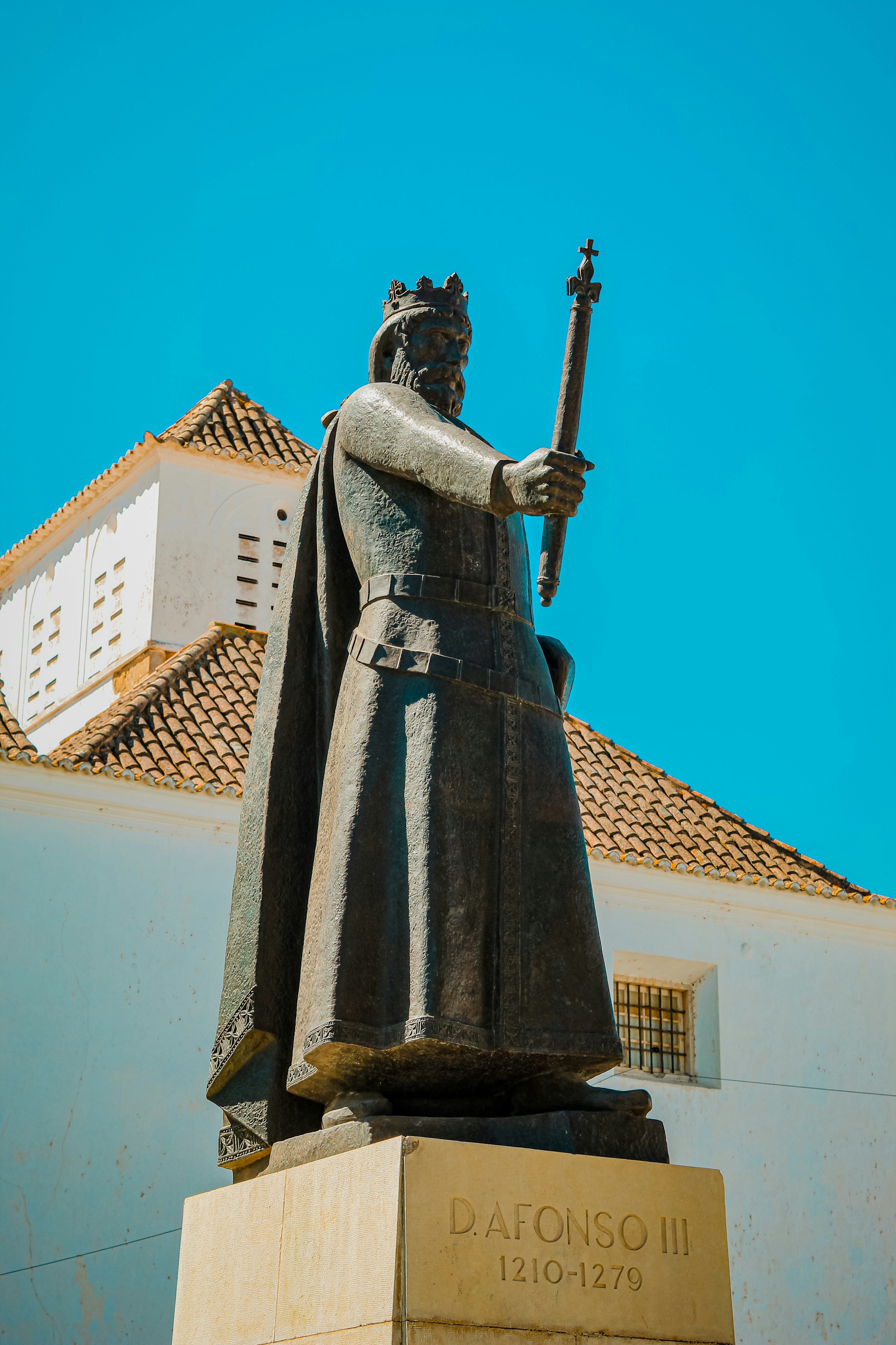 Bronze statue of King Afonso III holding a scepter before a white building