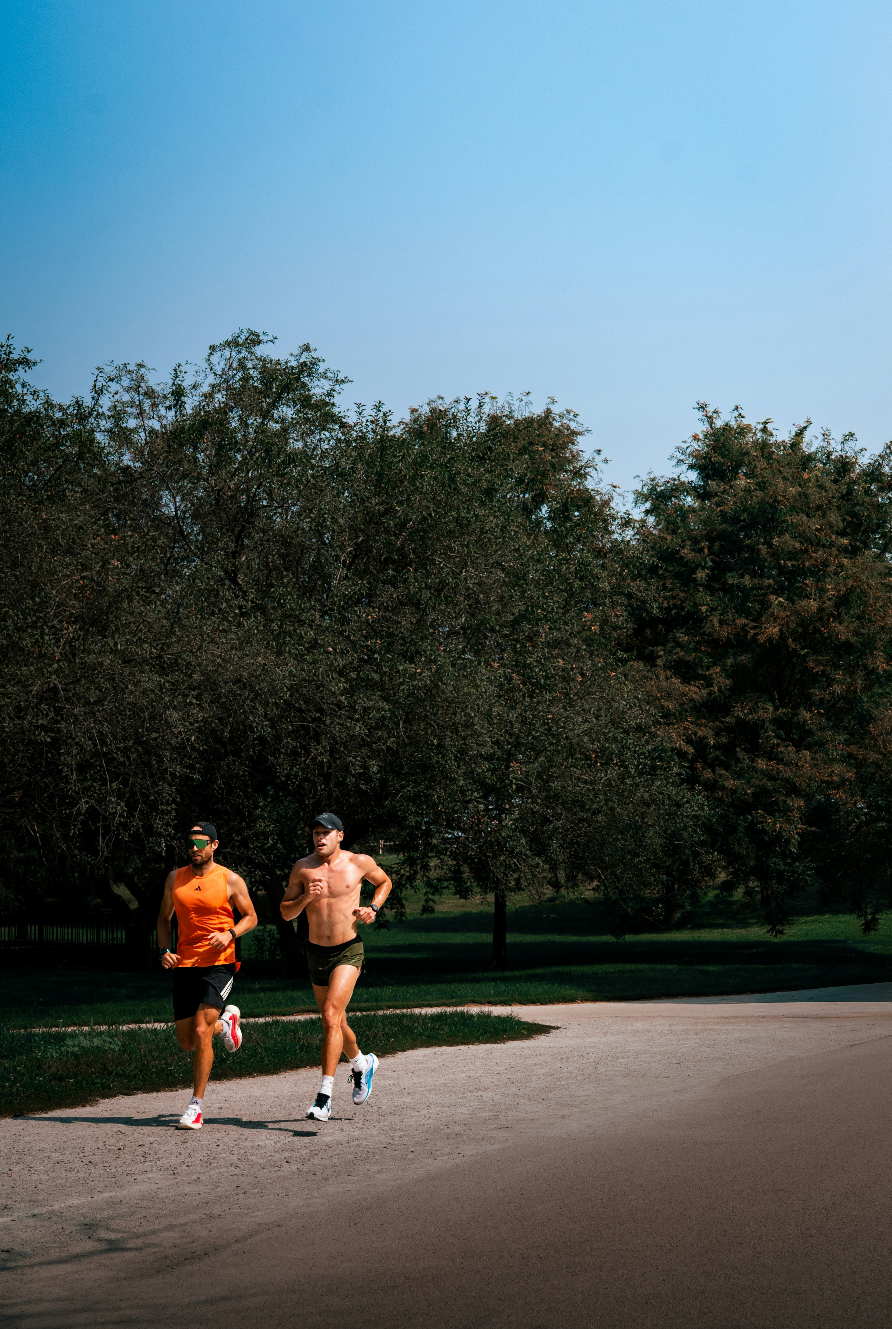 Two men running on a gravel path in a park with green trees