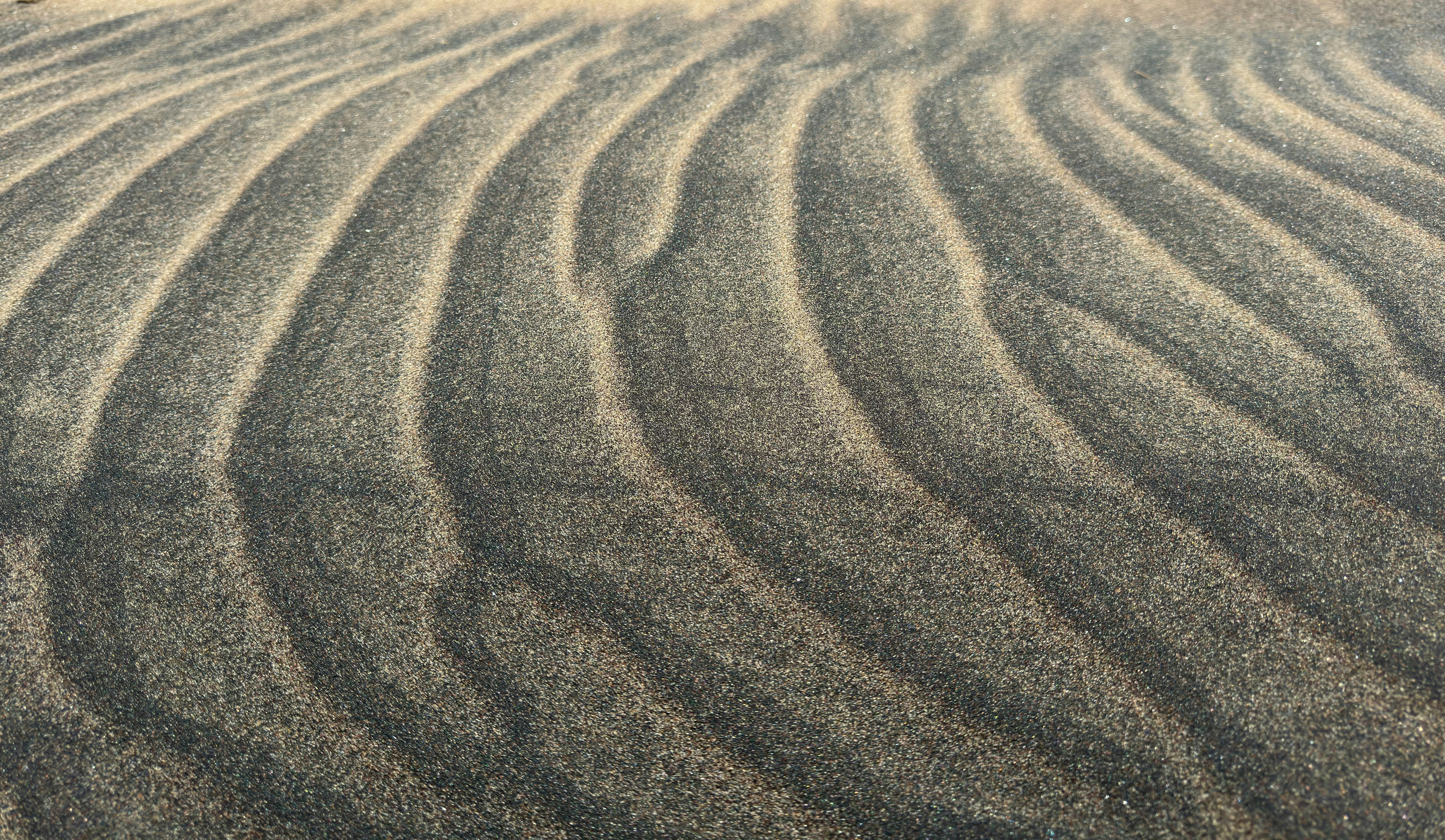 Rippled patterns of dark and light sand on a beach