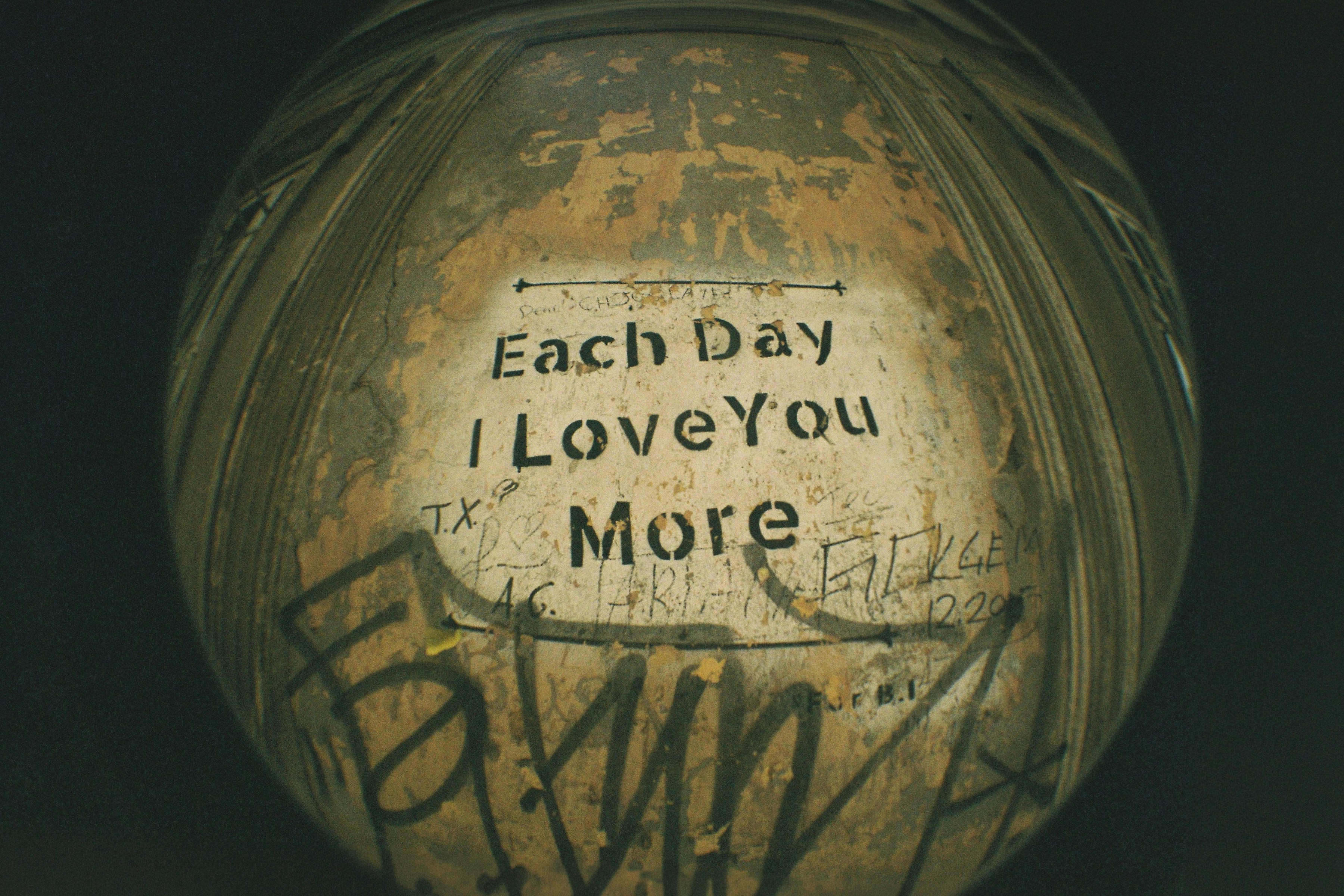 Stenciled text reading "Each Day I Love You More" on a weathered wall with graffiti