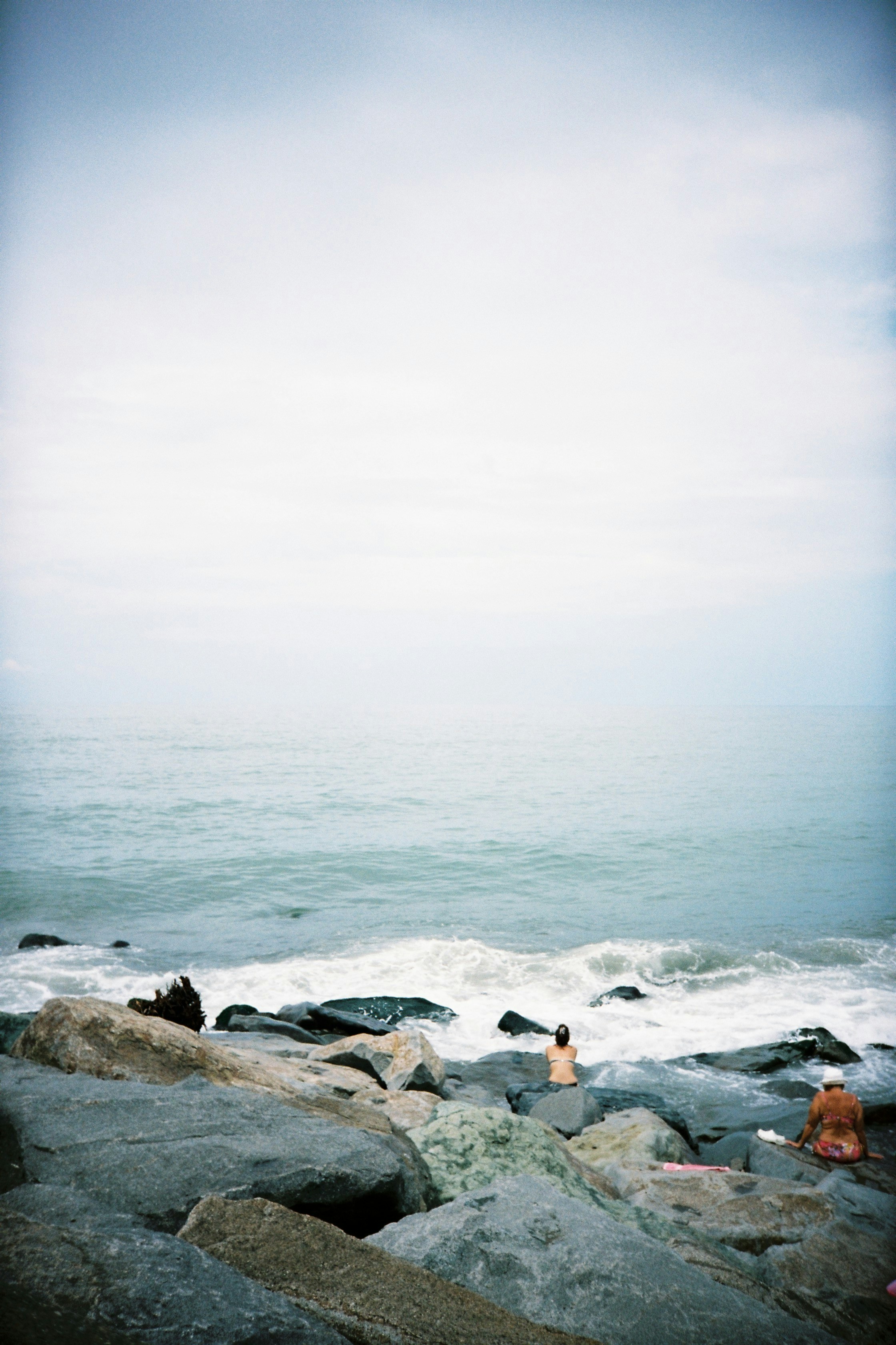 Two people on a rocky shoreline by the ocean under a cloudy sky