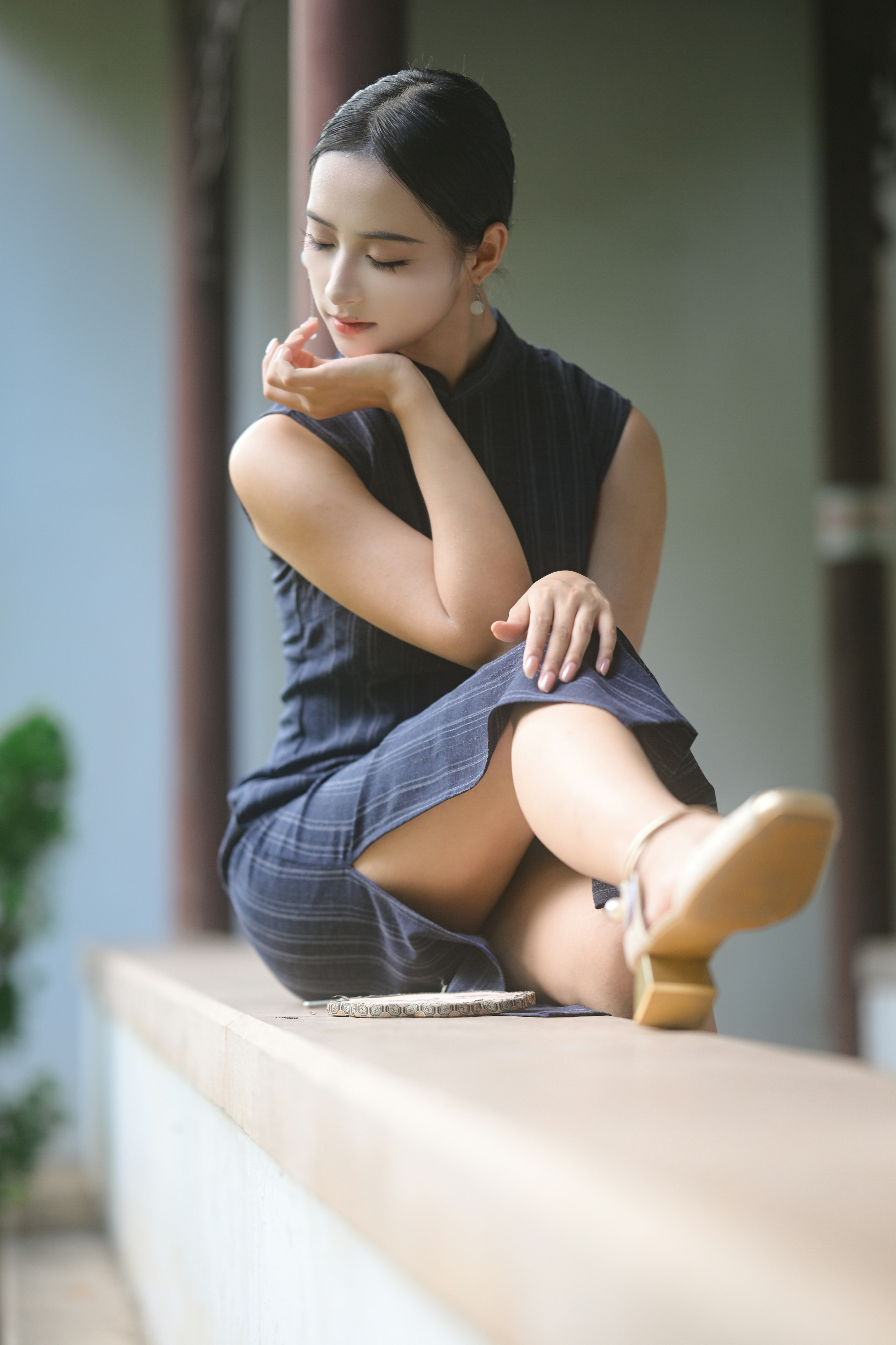 A woman in a dark pinstriped dress resting on a stone ledge