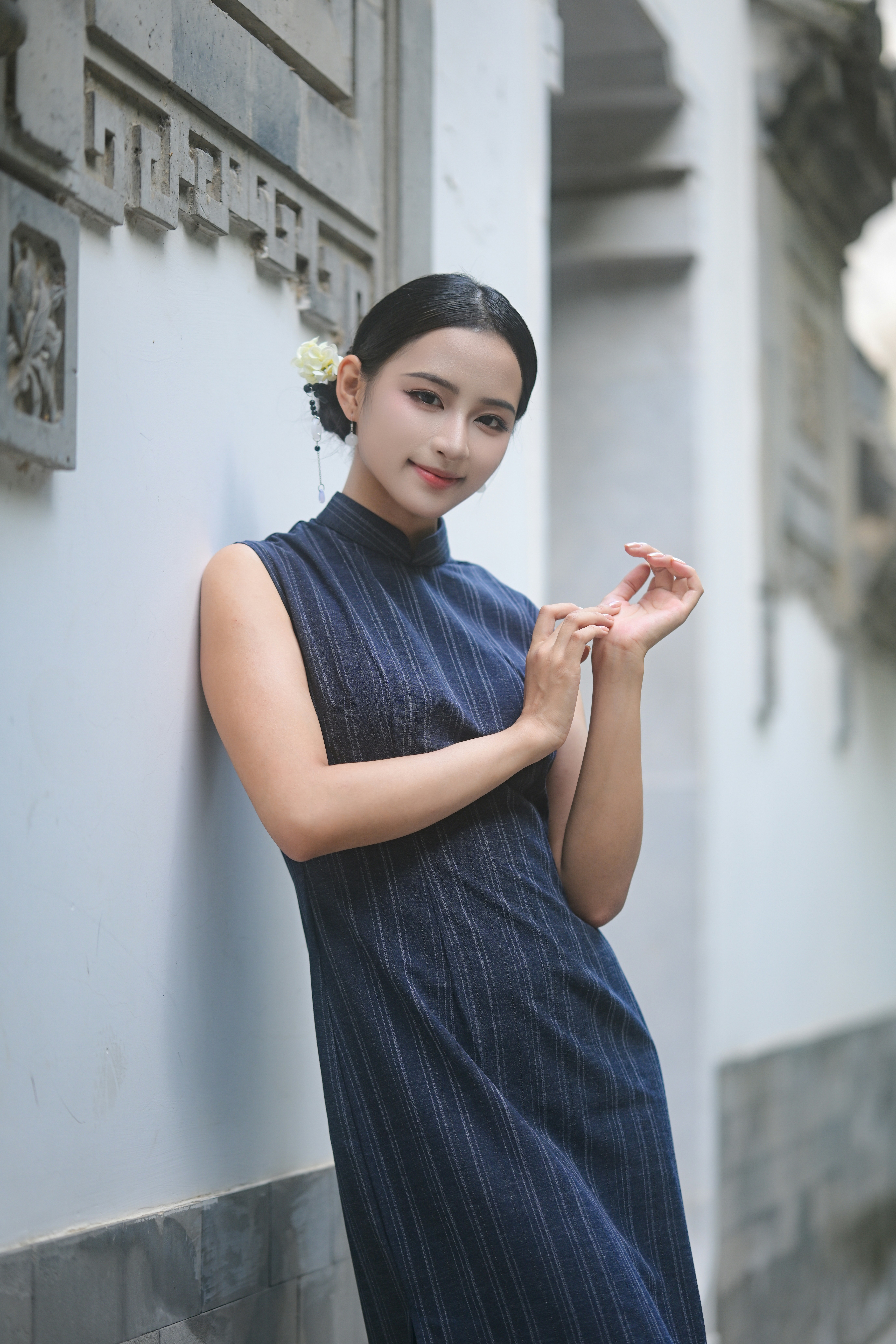 A woman in a blue pinstriped cheongsam leaning against a white wall