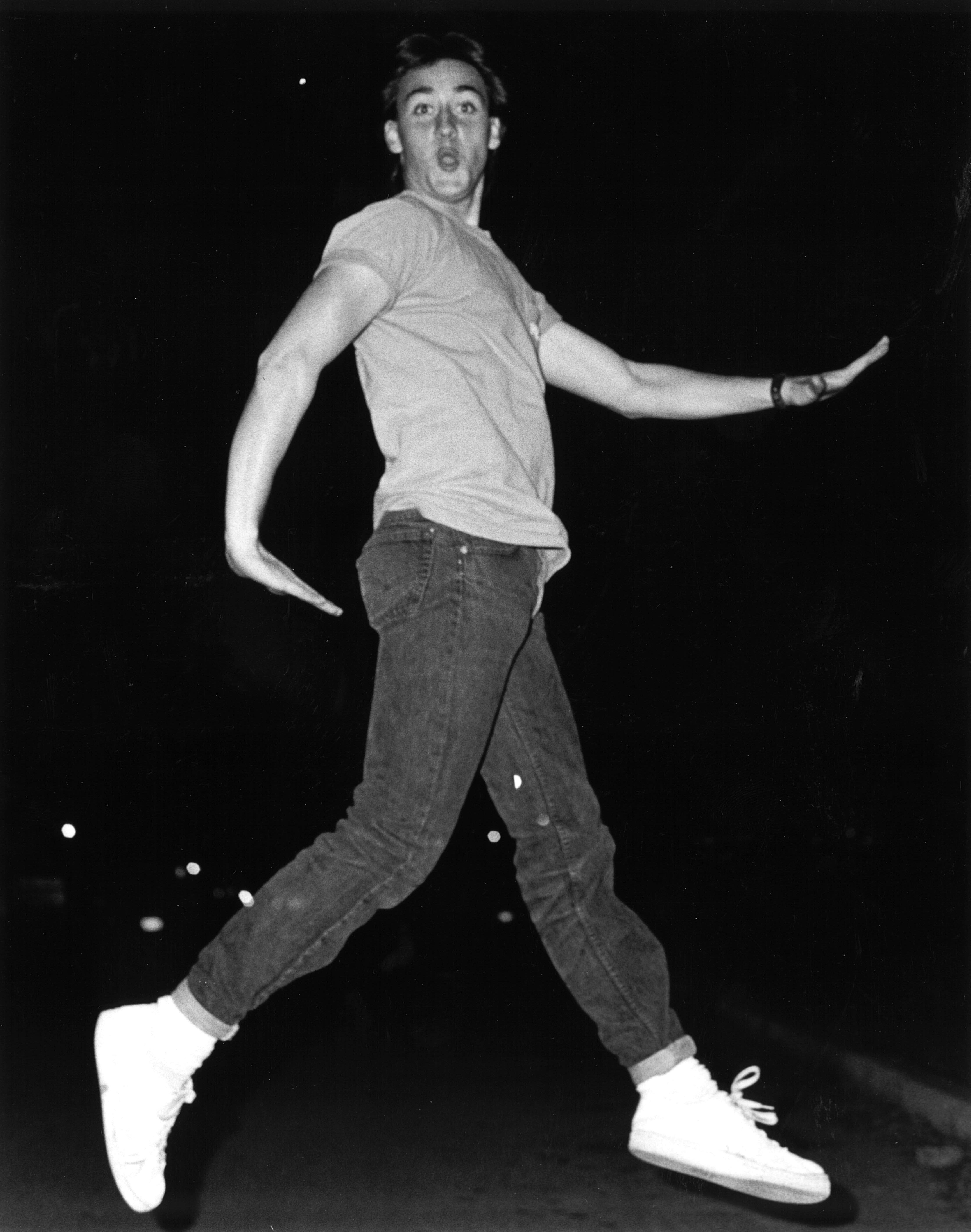 A man in a t-shirt and jeans jumping against a dark background