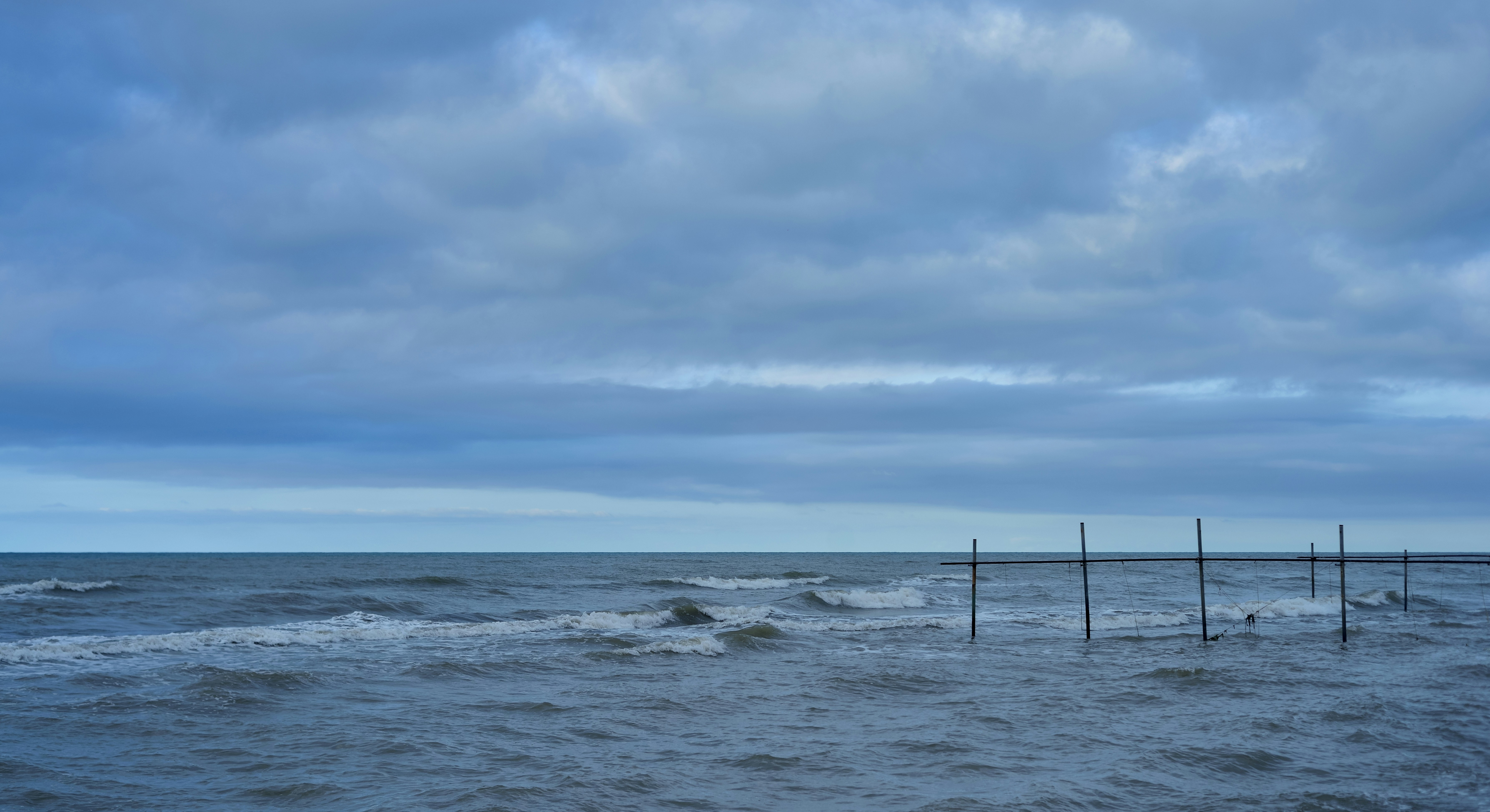 Holzstangen im Meer unter einem schweren, bewölkten Himmel mit rollenden Wellen