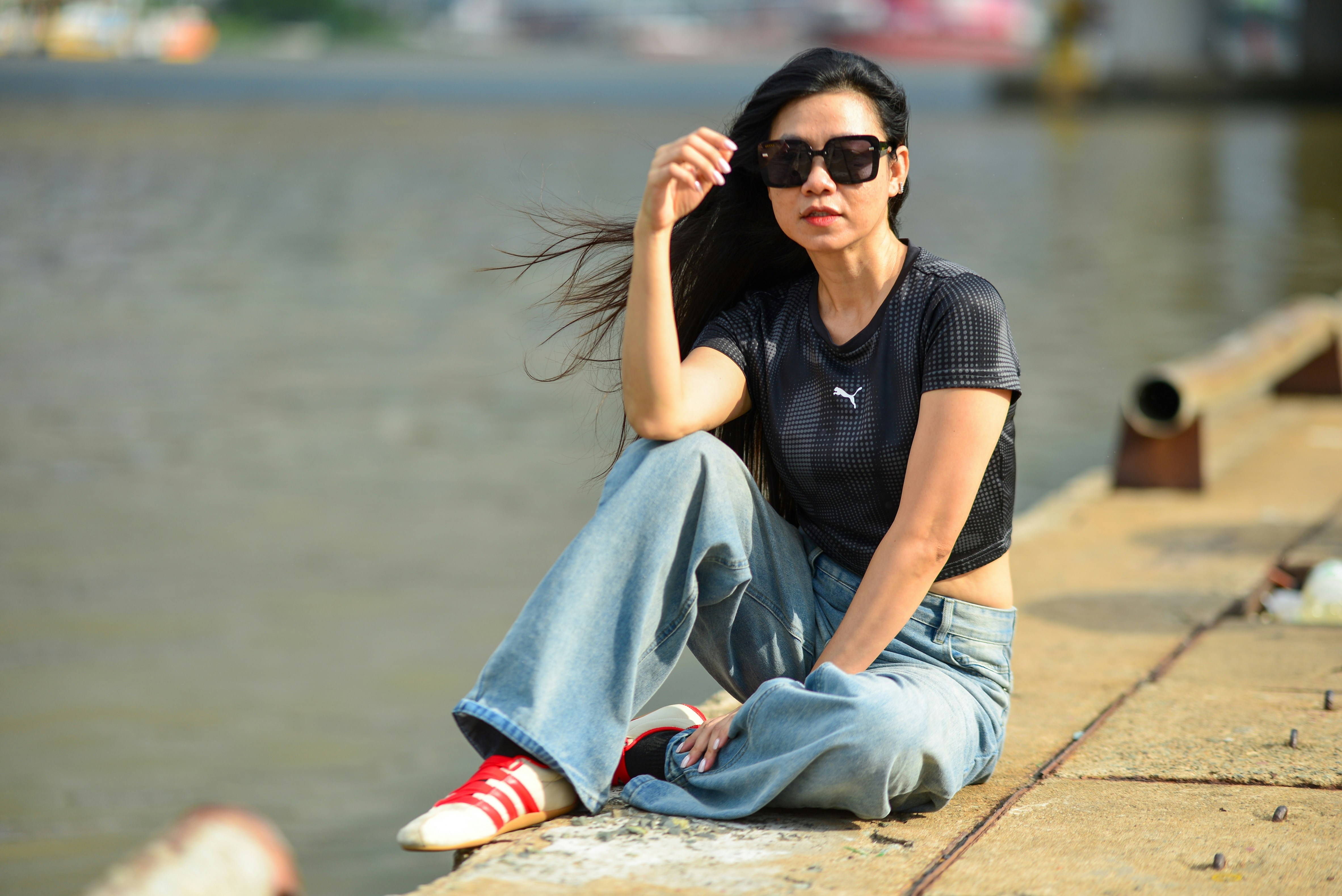 A woman in a black t-shirt and blue jeans sitting on a concrete pier