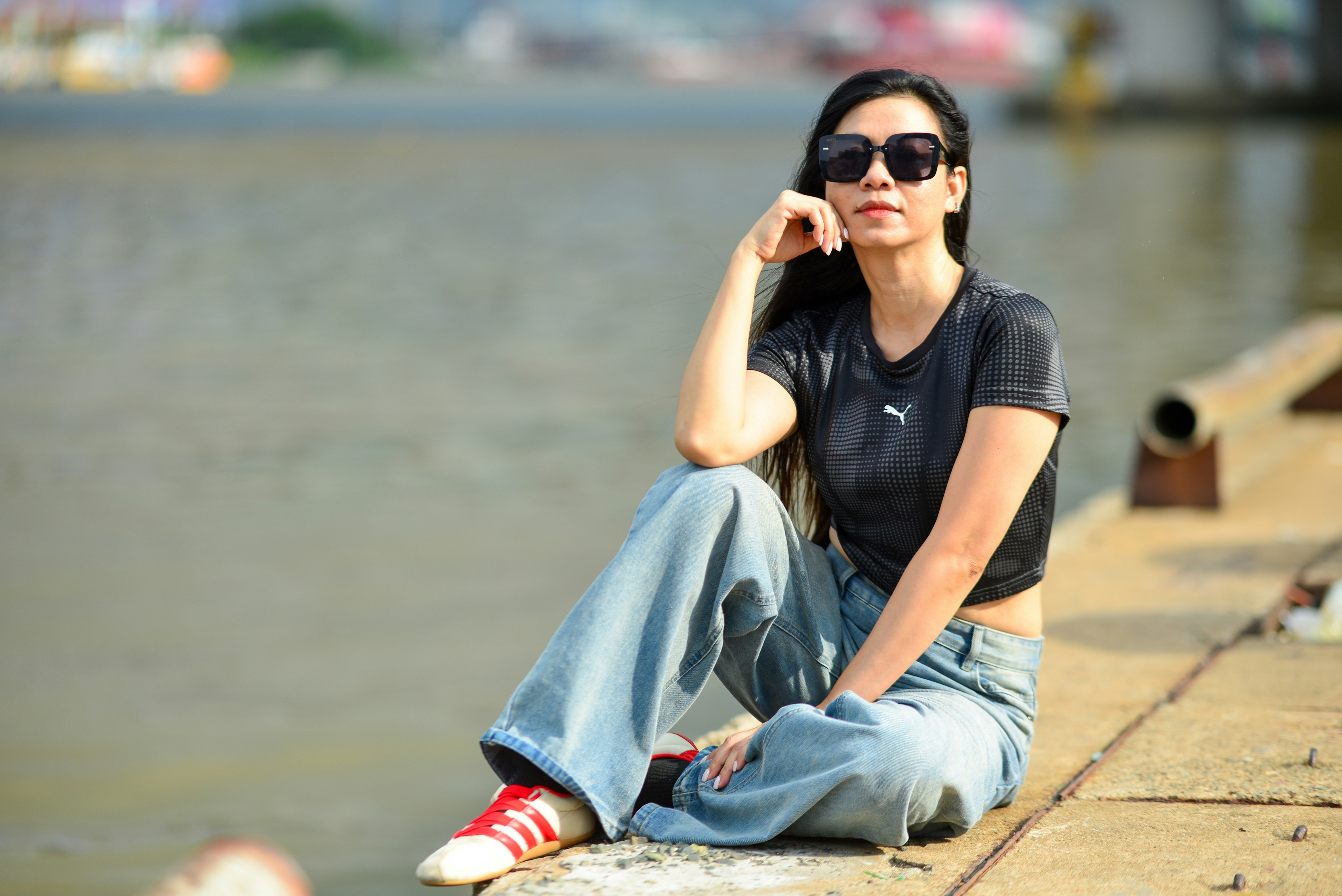A woman in a black crop top and wide-leg jeans sitting by water