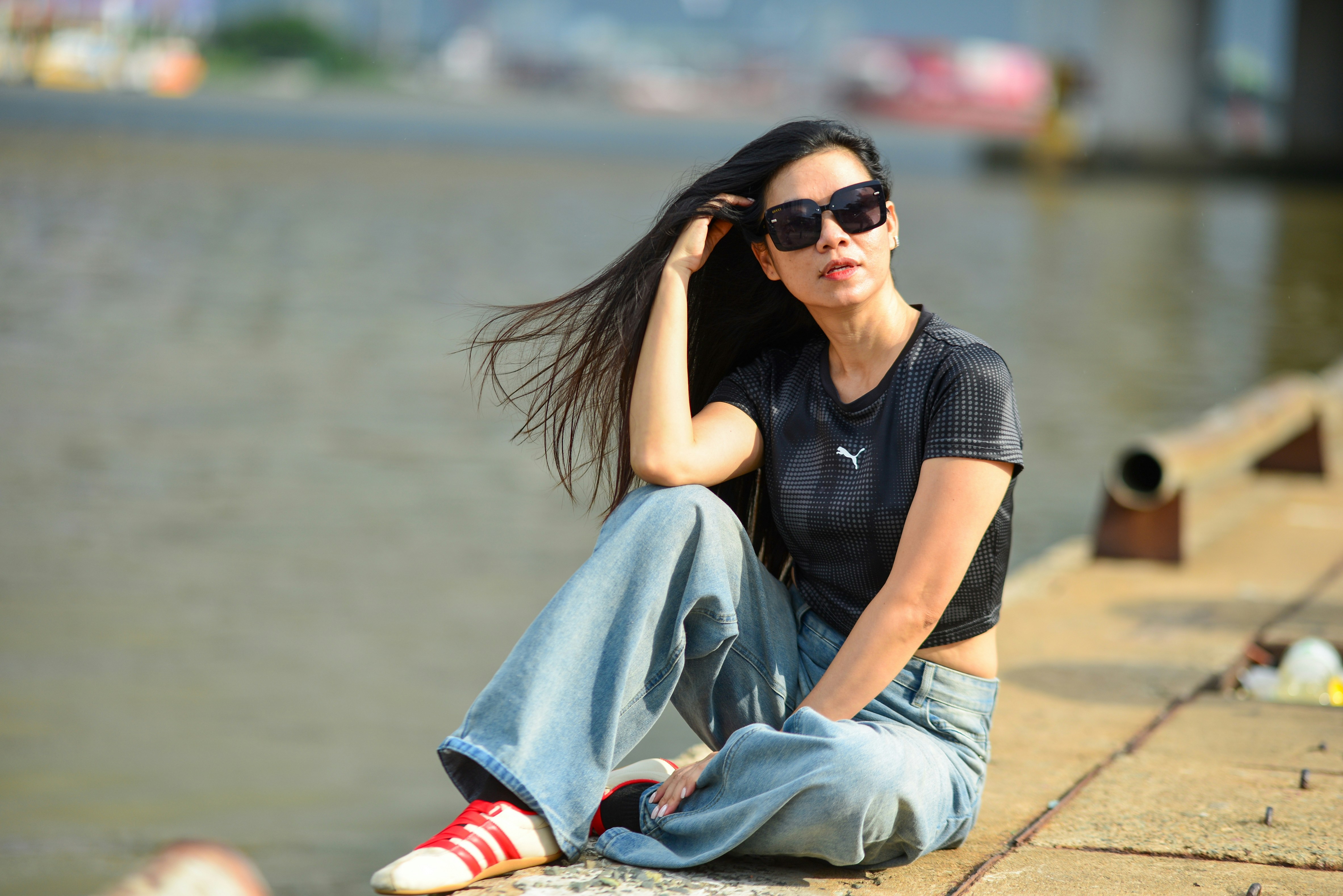 A woman in sunglasses and a black crop top sitting on a concrete pier