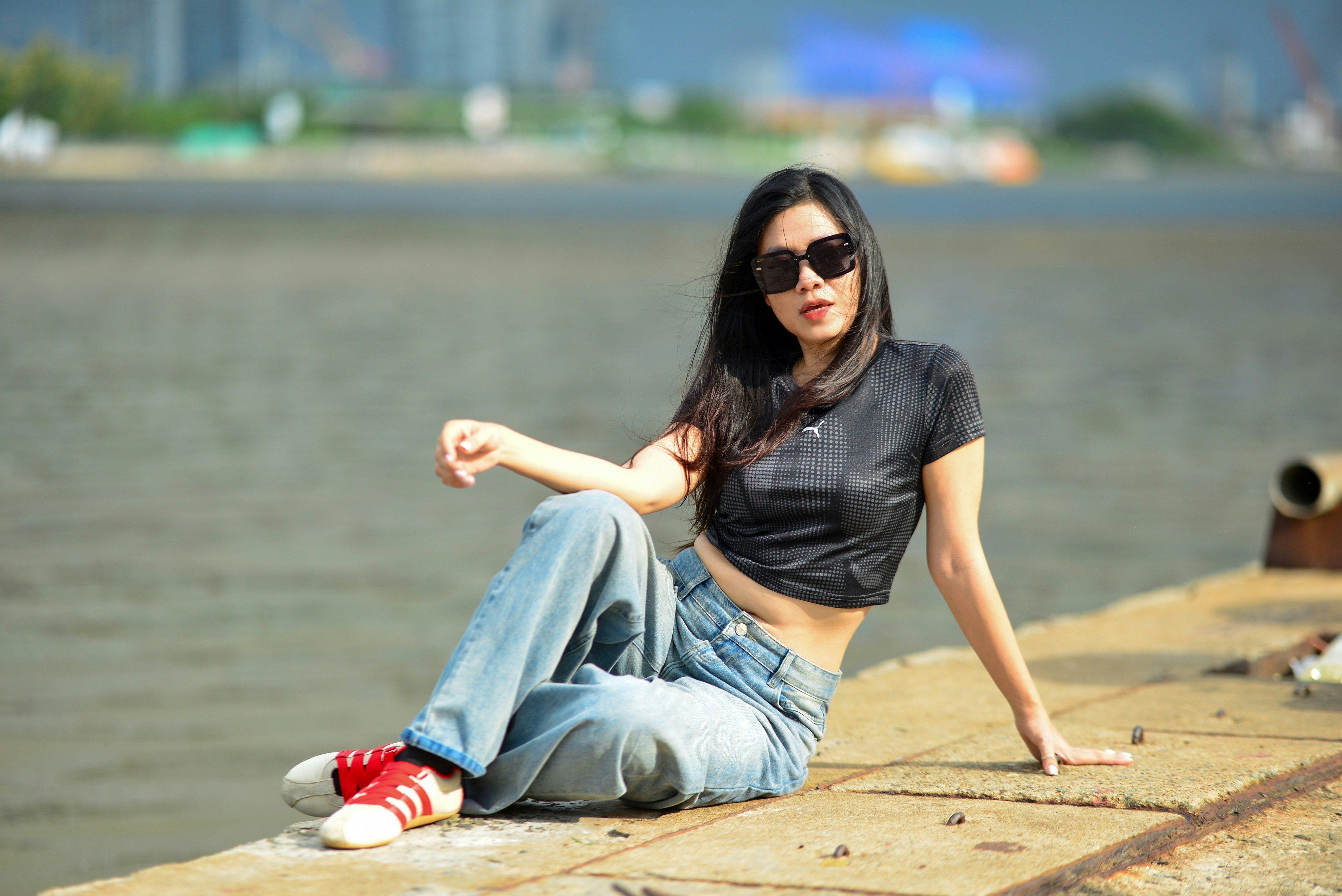 A woman in a black crop top and jeans sitting on a concrete pier