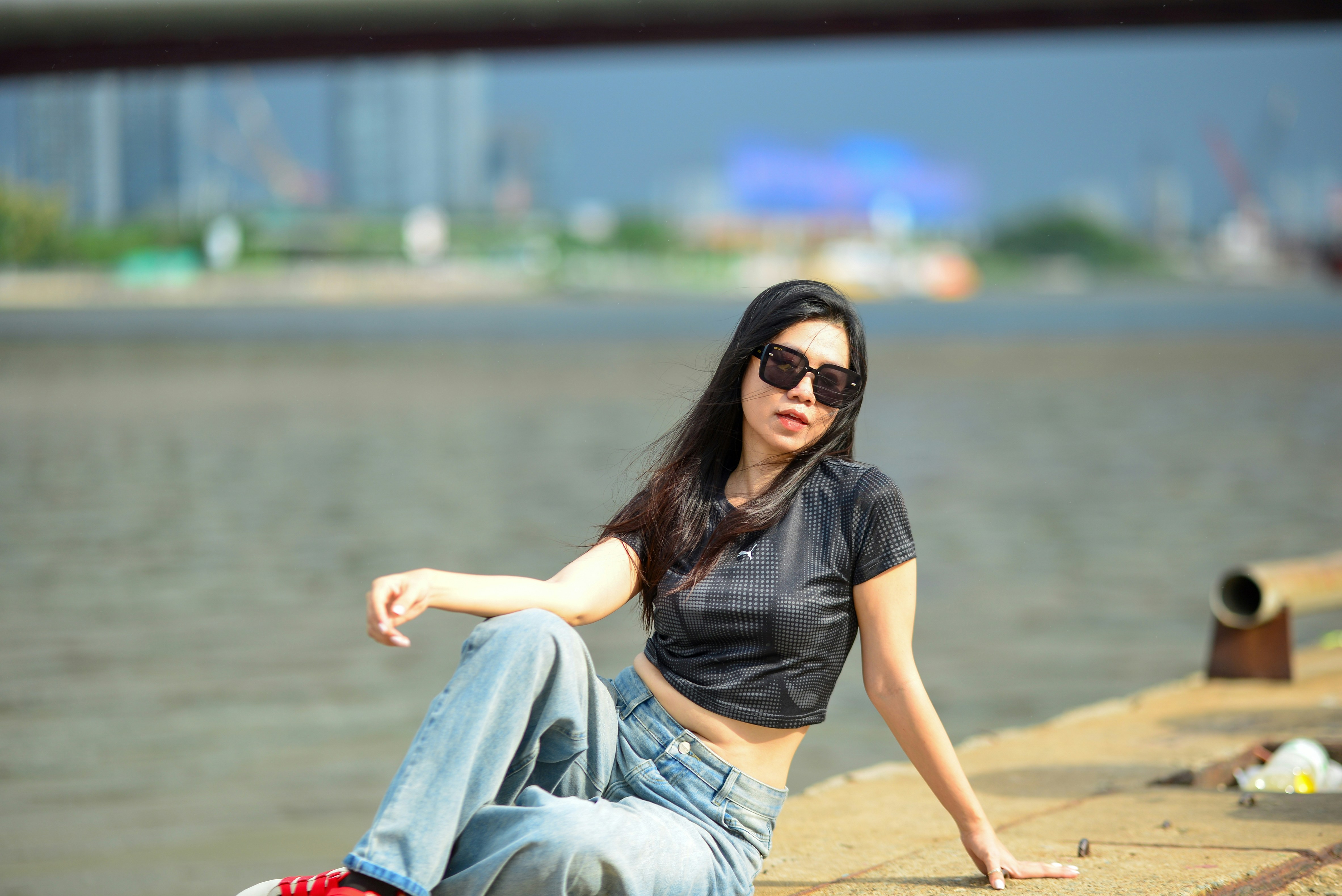 A woman in a black crop top and jeans sitting by a river