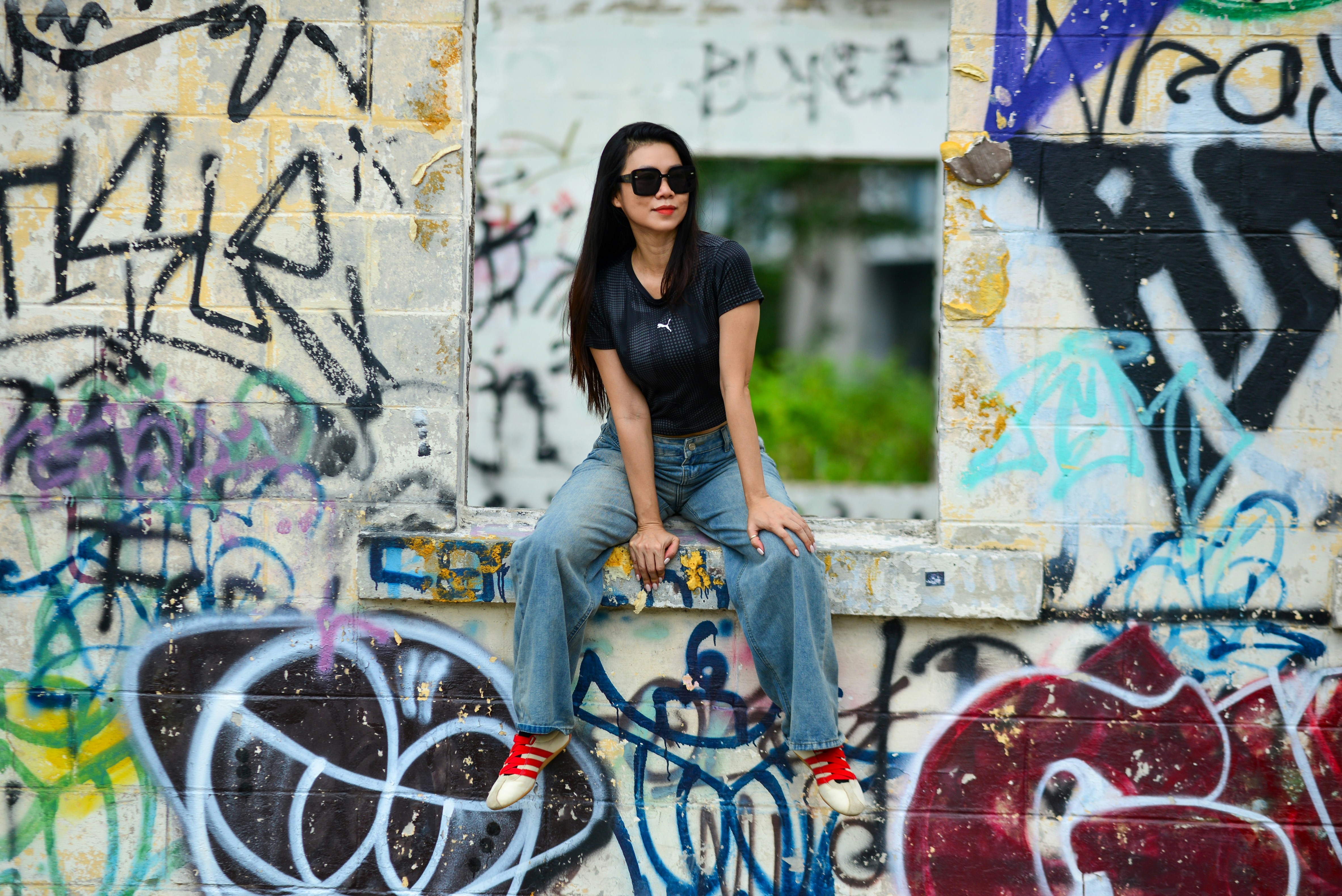 A woman in a black t-shirt and jeans sitting on a graffiti-covered wall
