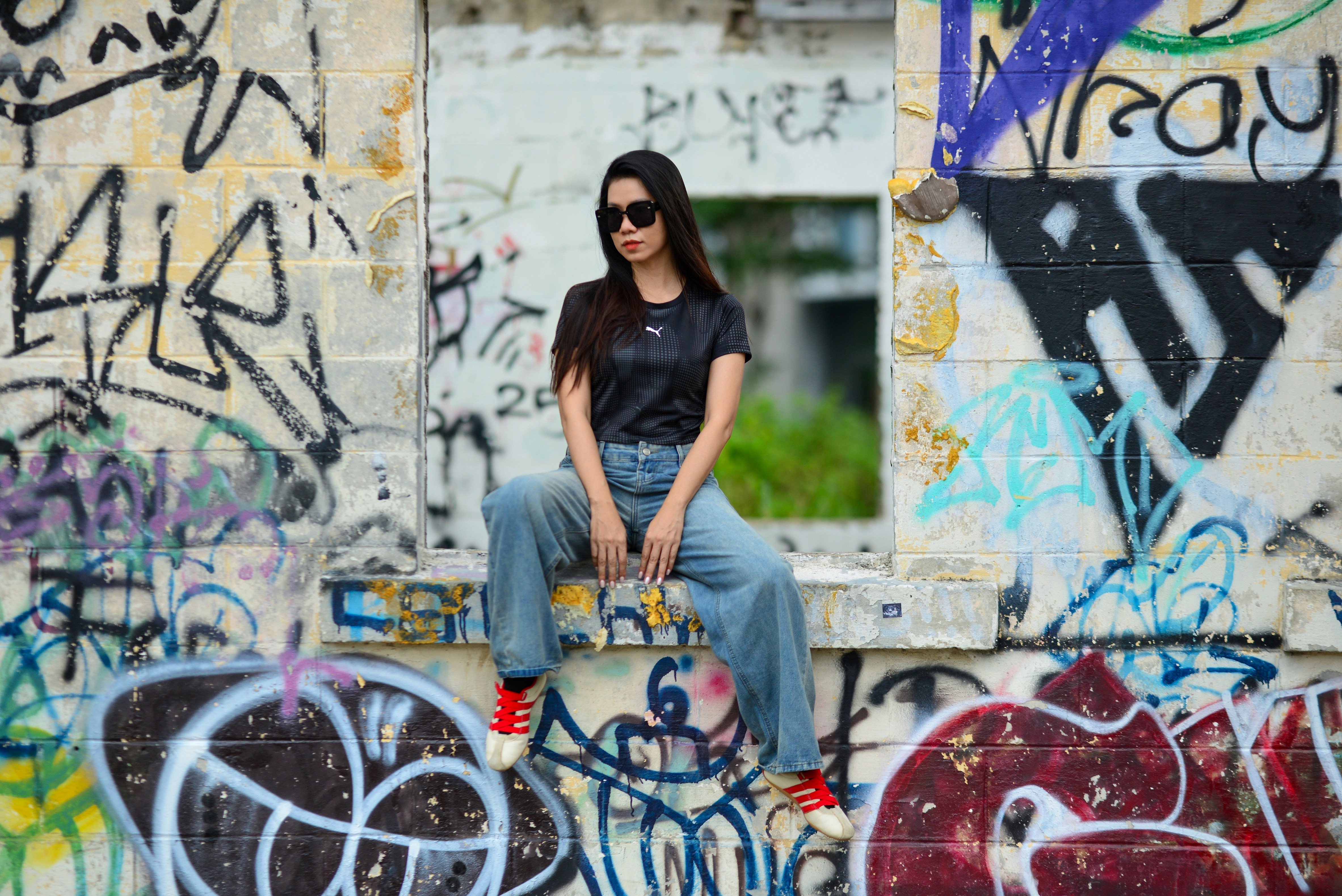 A woman in sunglasses and a black shirt sitting on a graffiti-covered wall