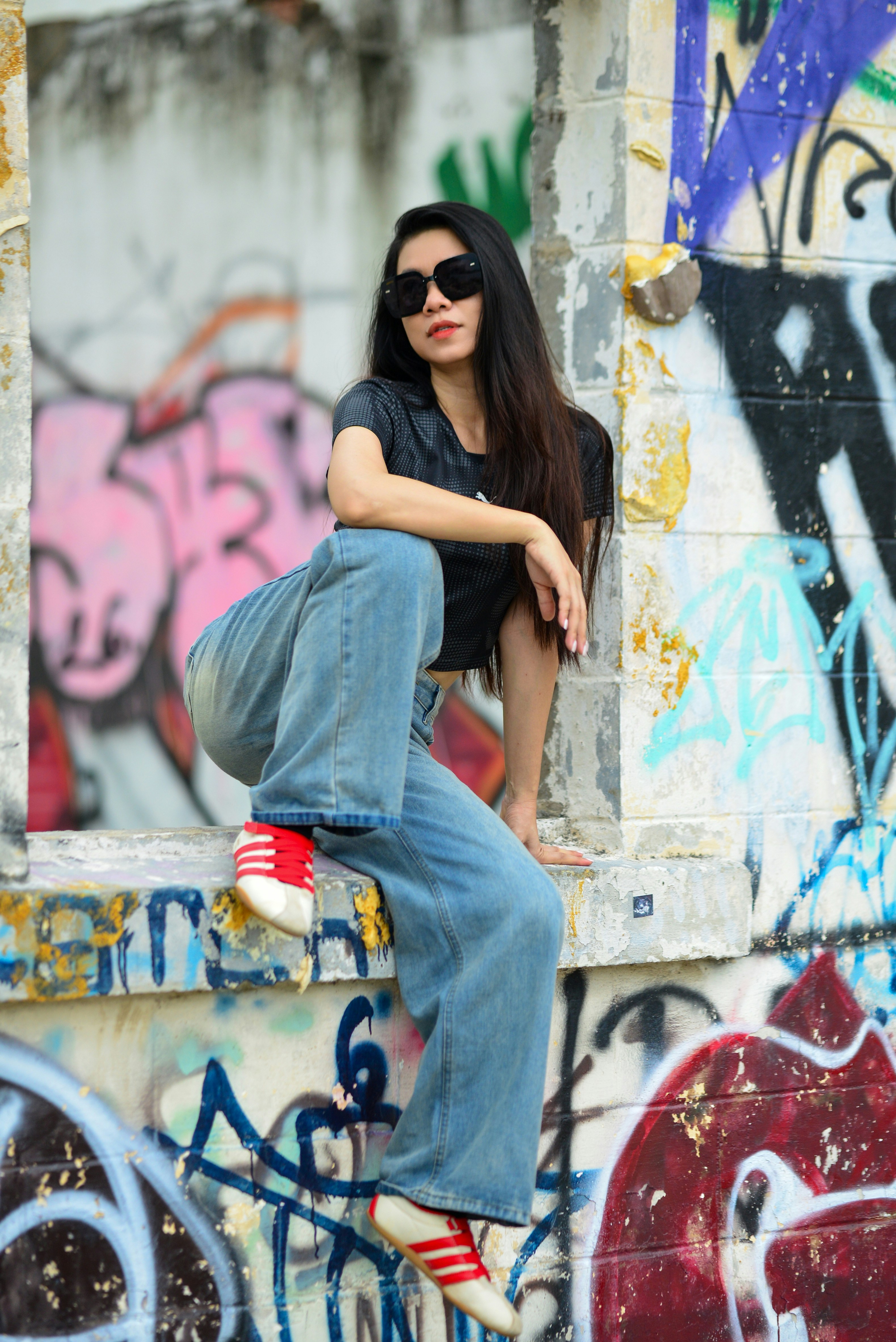 A woman in sunglasses and a black top sitting on a graffiti-covered wall