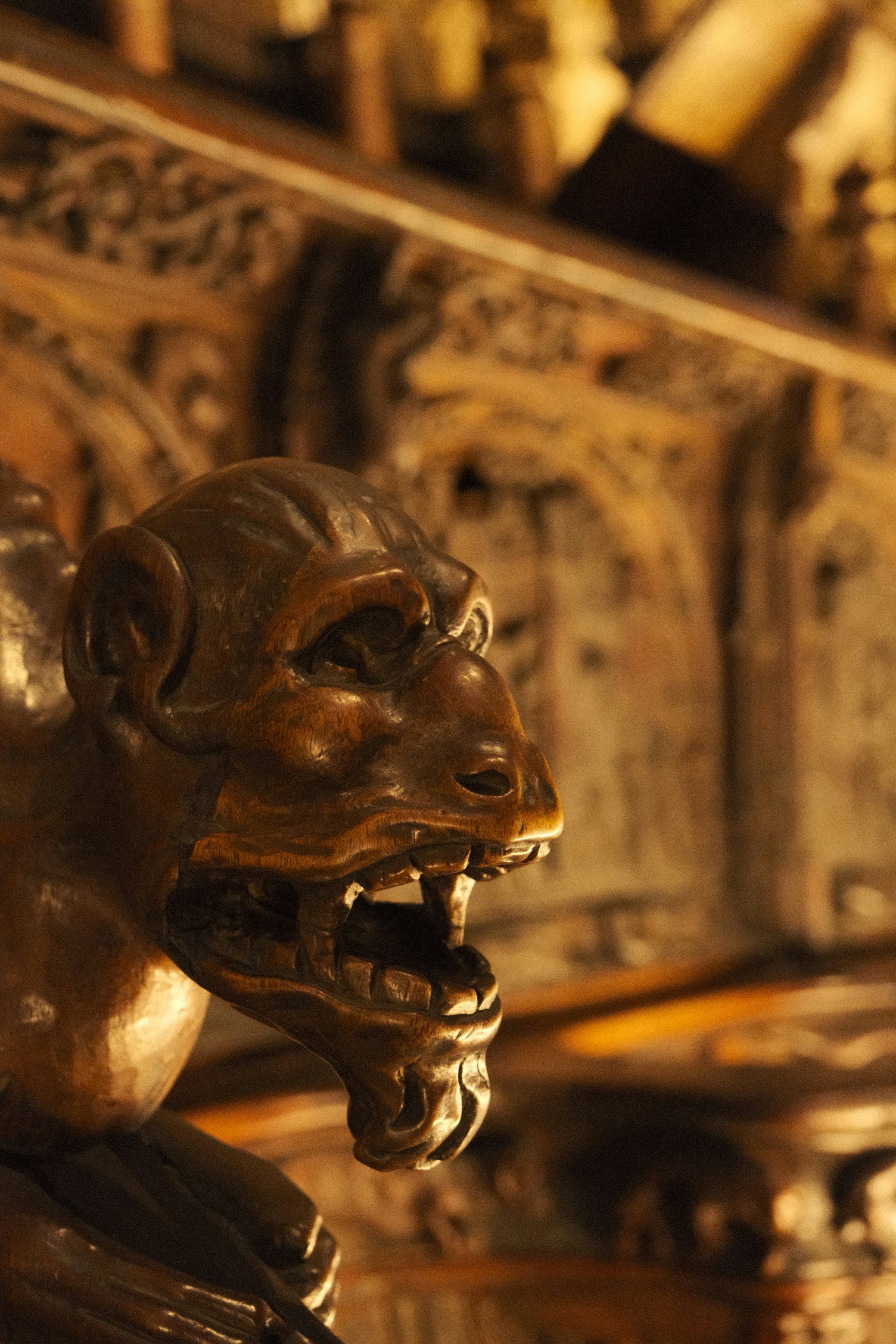 A carved wooden gargoyle head with an open mouth and sharp teeth