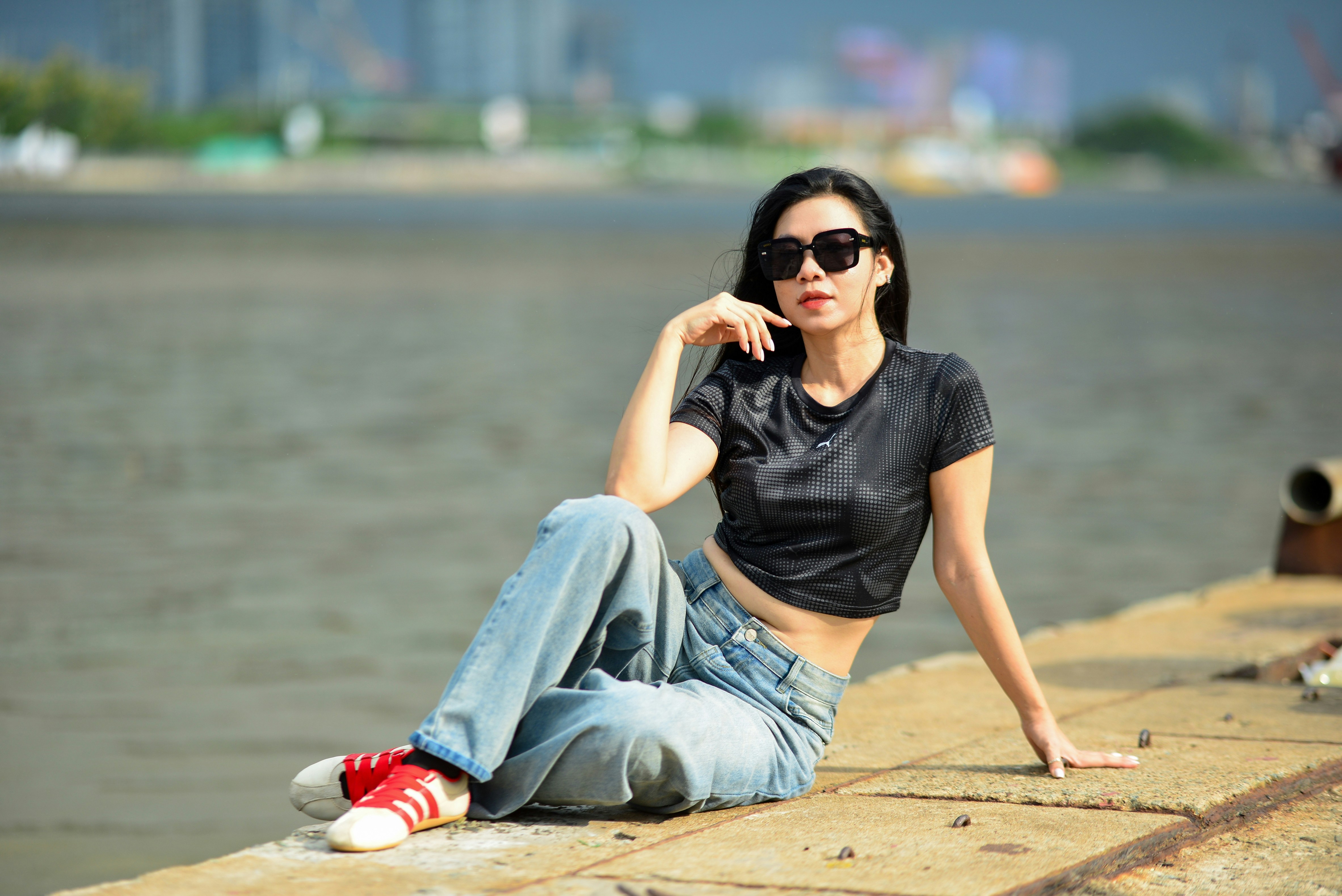 A woman in a black crop top and jeans sitting on a concrete pier