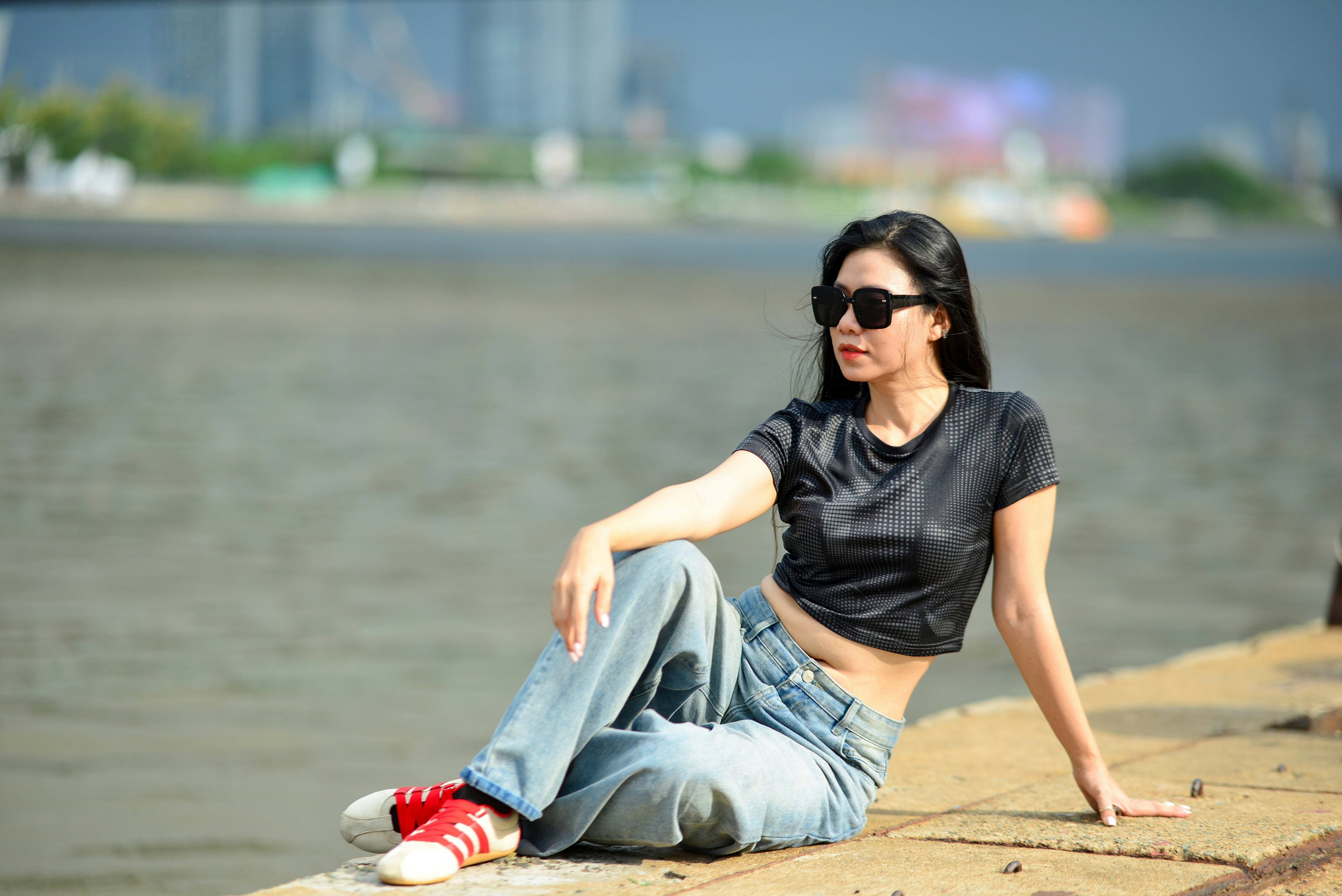 A woman in a black crop top and jeans sitting by a river
