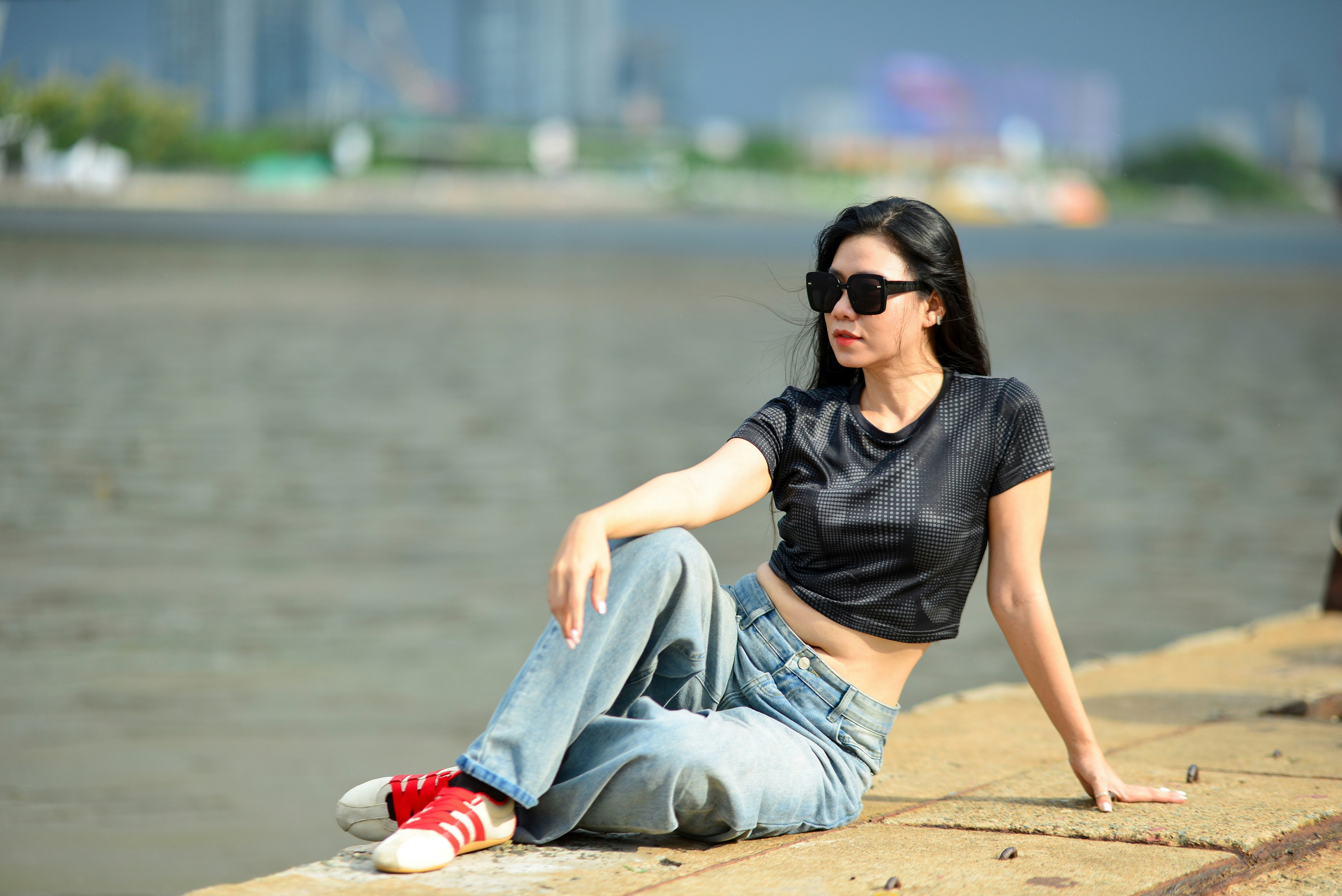 A woman in a black crop top and jeans sitting on a concrete pier