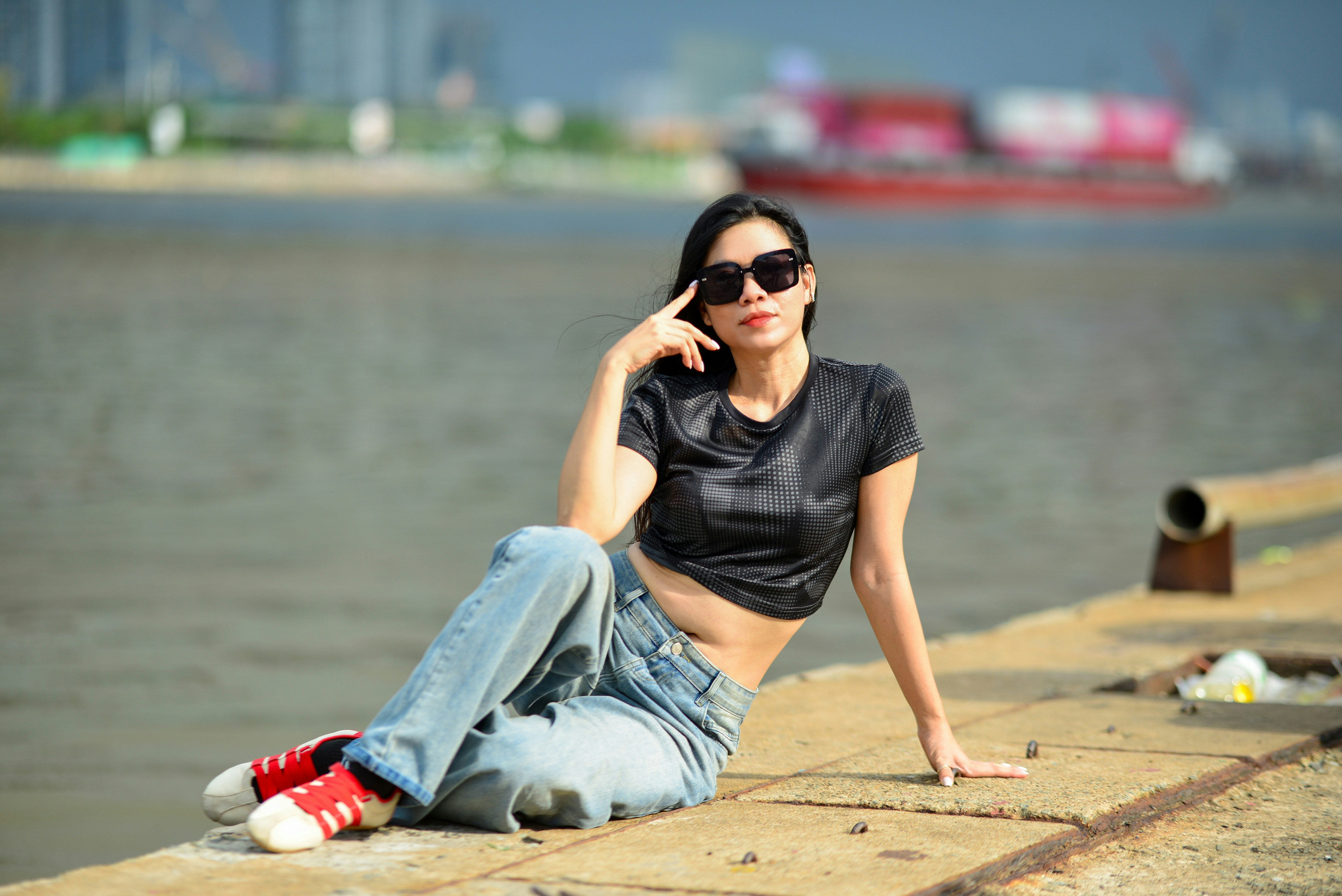 A woman in a black crop top and jeans sitting on a concrete pier