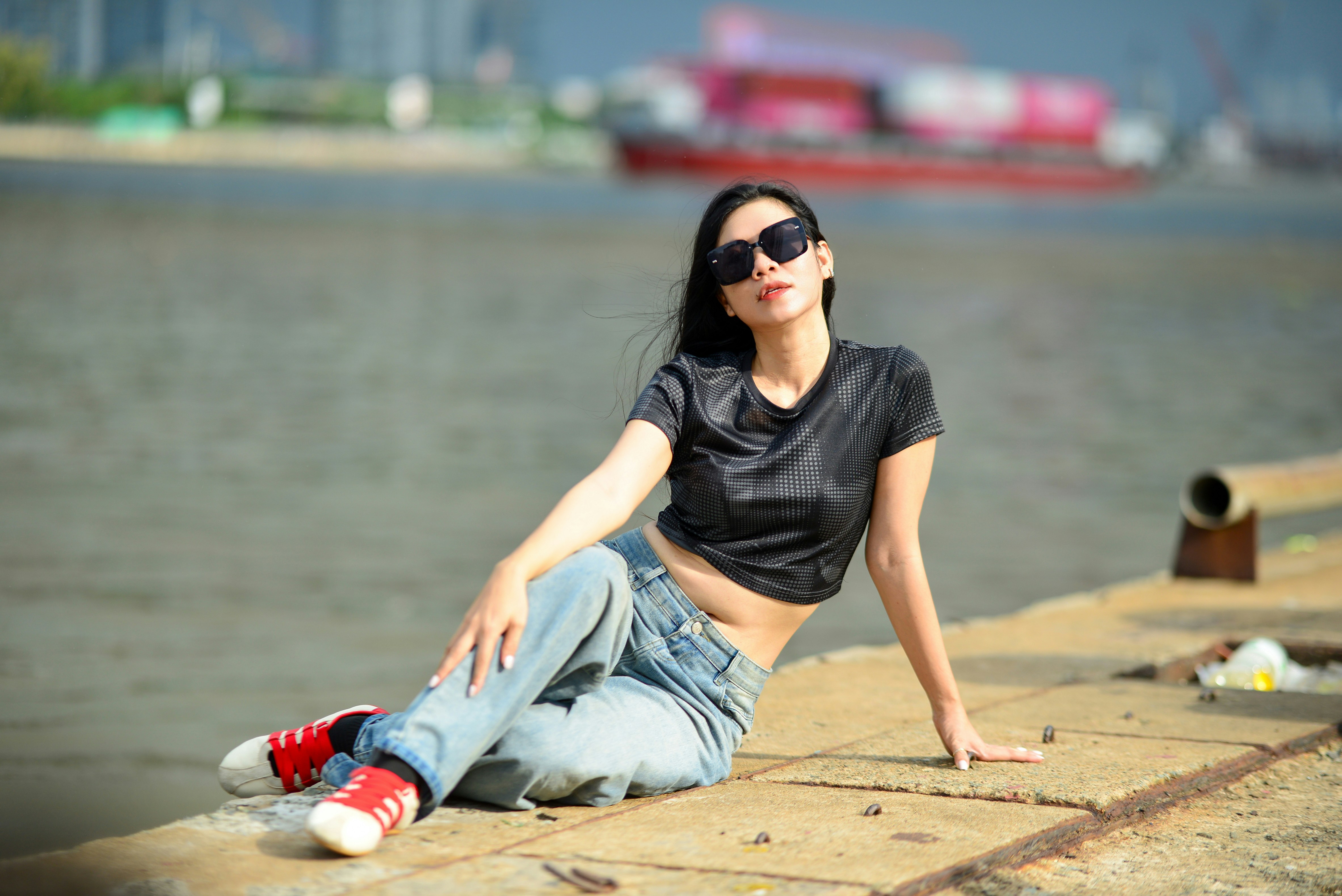 A woman in a black crop top and jeans sitting on a concrete pier