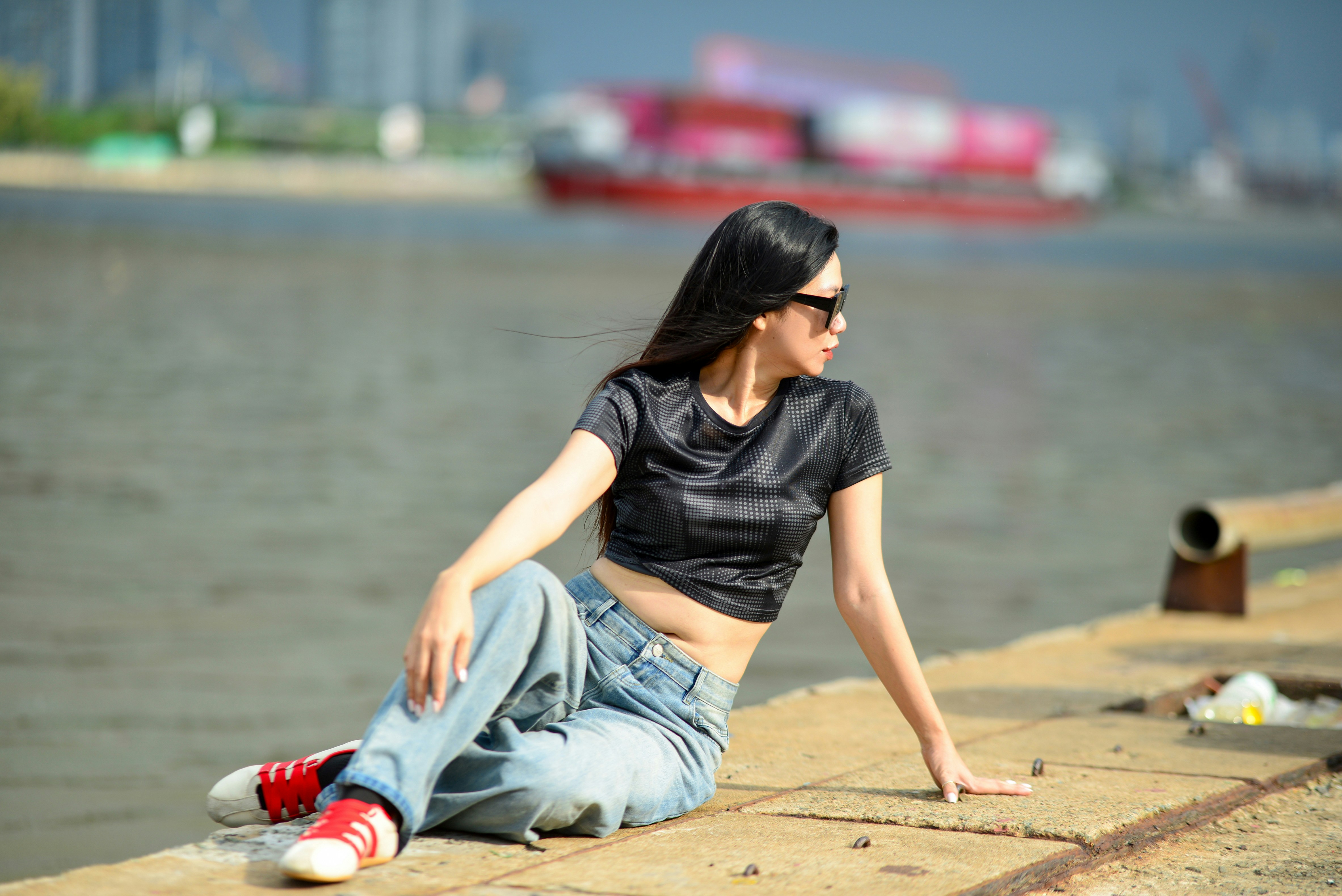 A woman in a black crop top and jeans sitting on a concrete pier