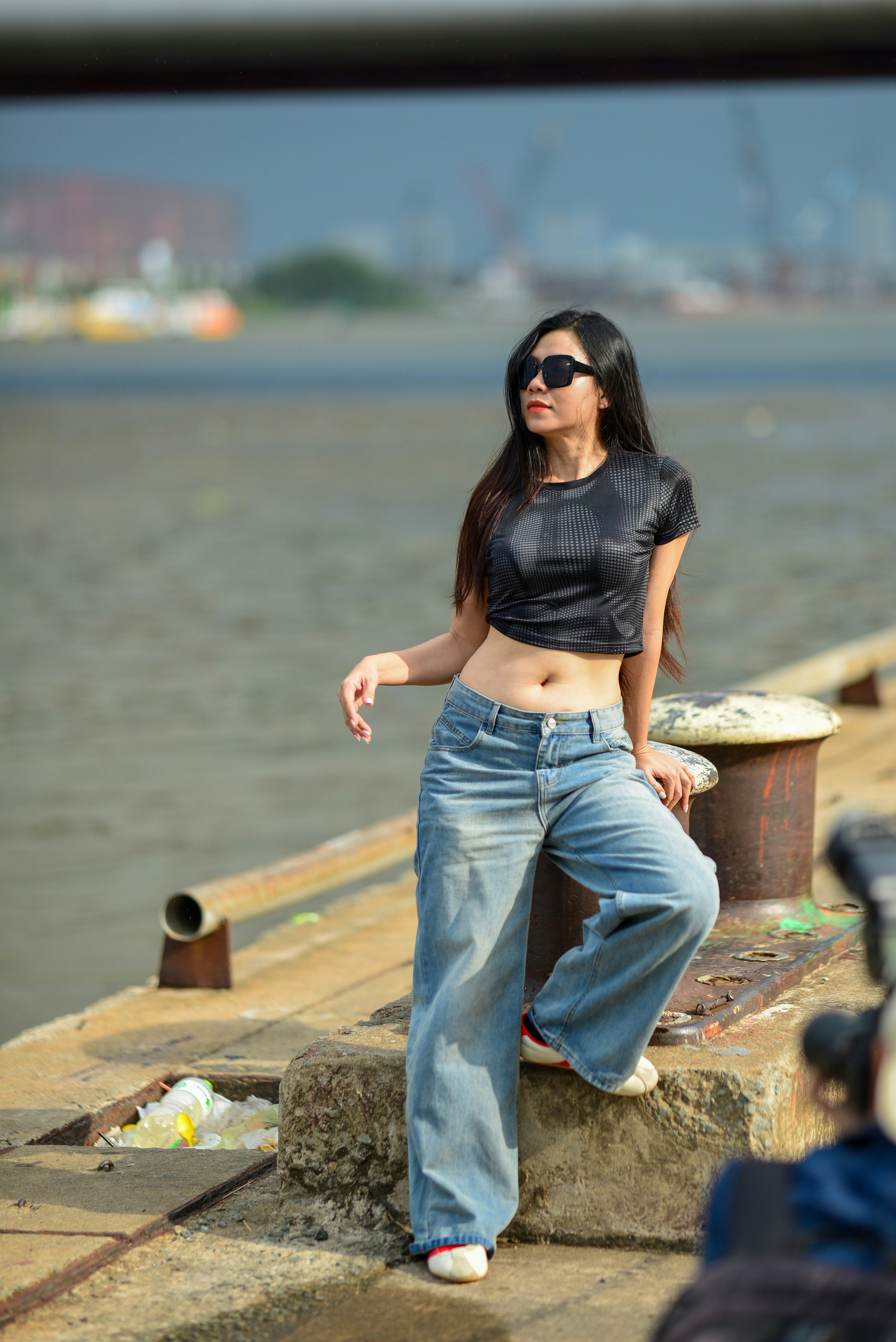 A woman in a black crop top and jeans leaning against a dock bollard