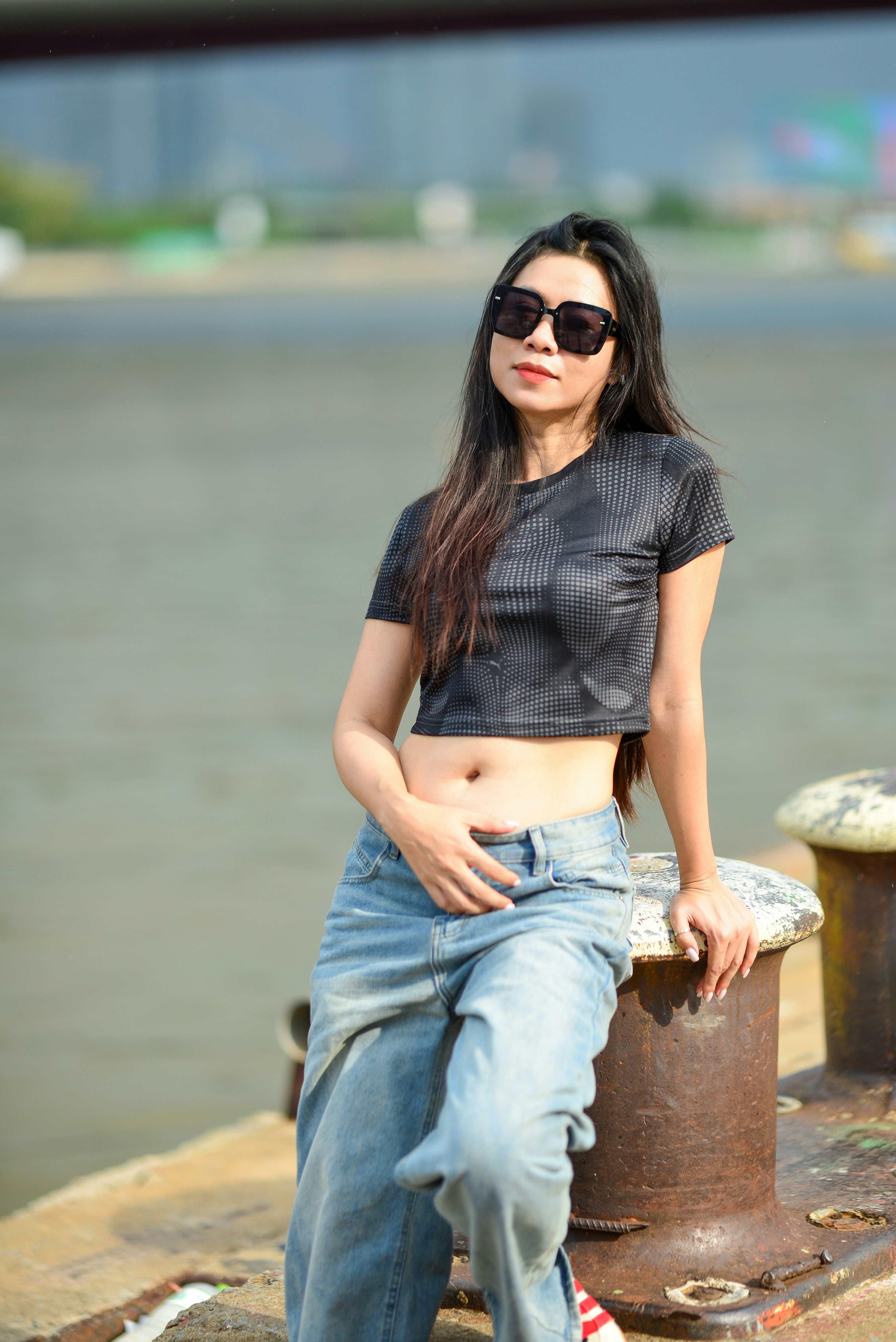 A woman in a black crop top and jeans leaning against a metal bollard