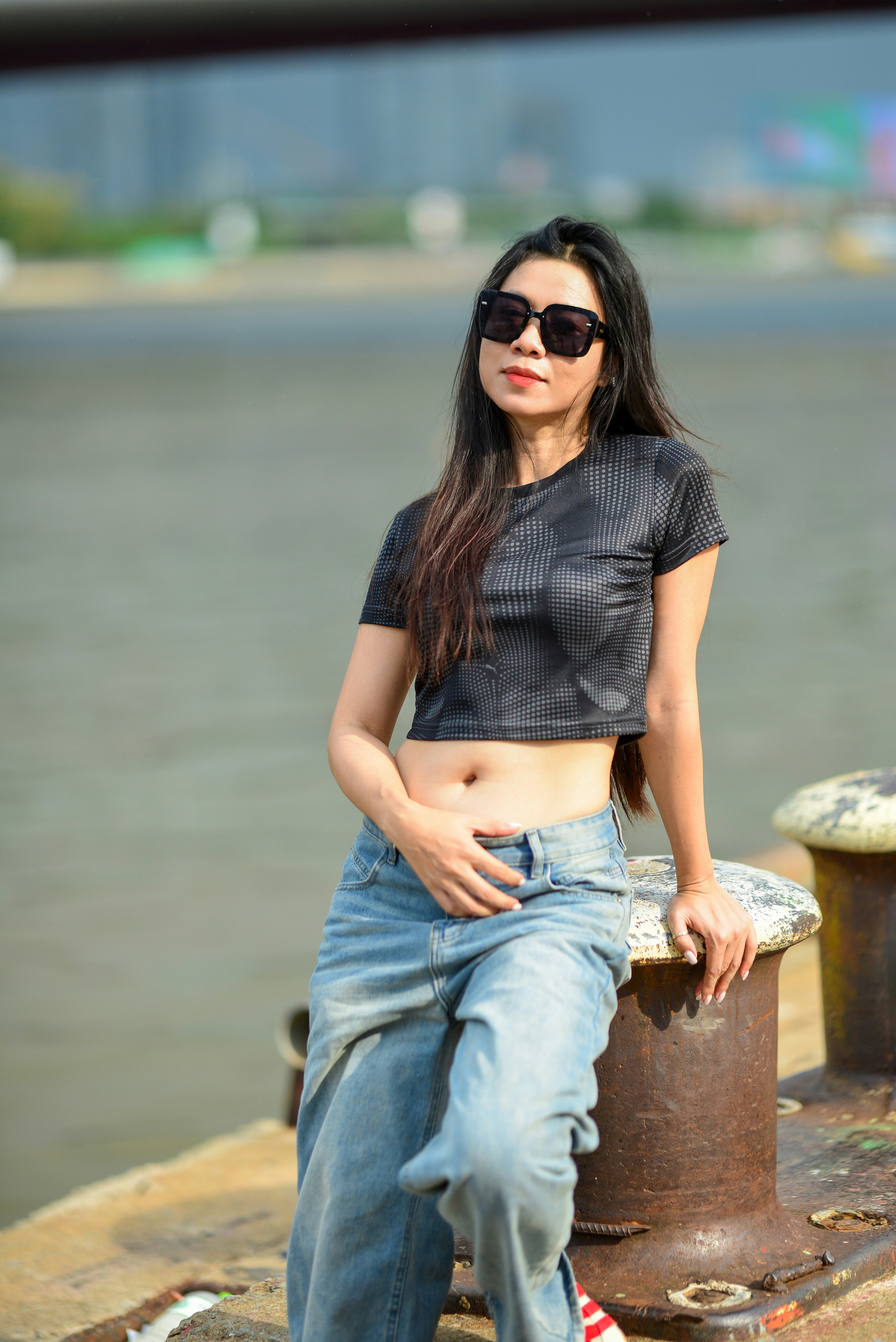 A woman in a black crop top and jeans leaning against a metal bollard