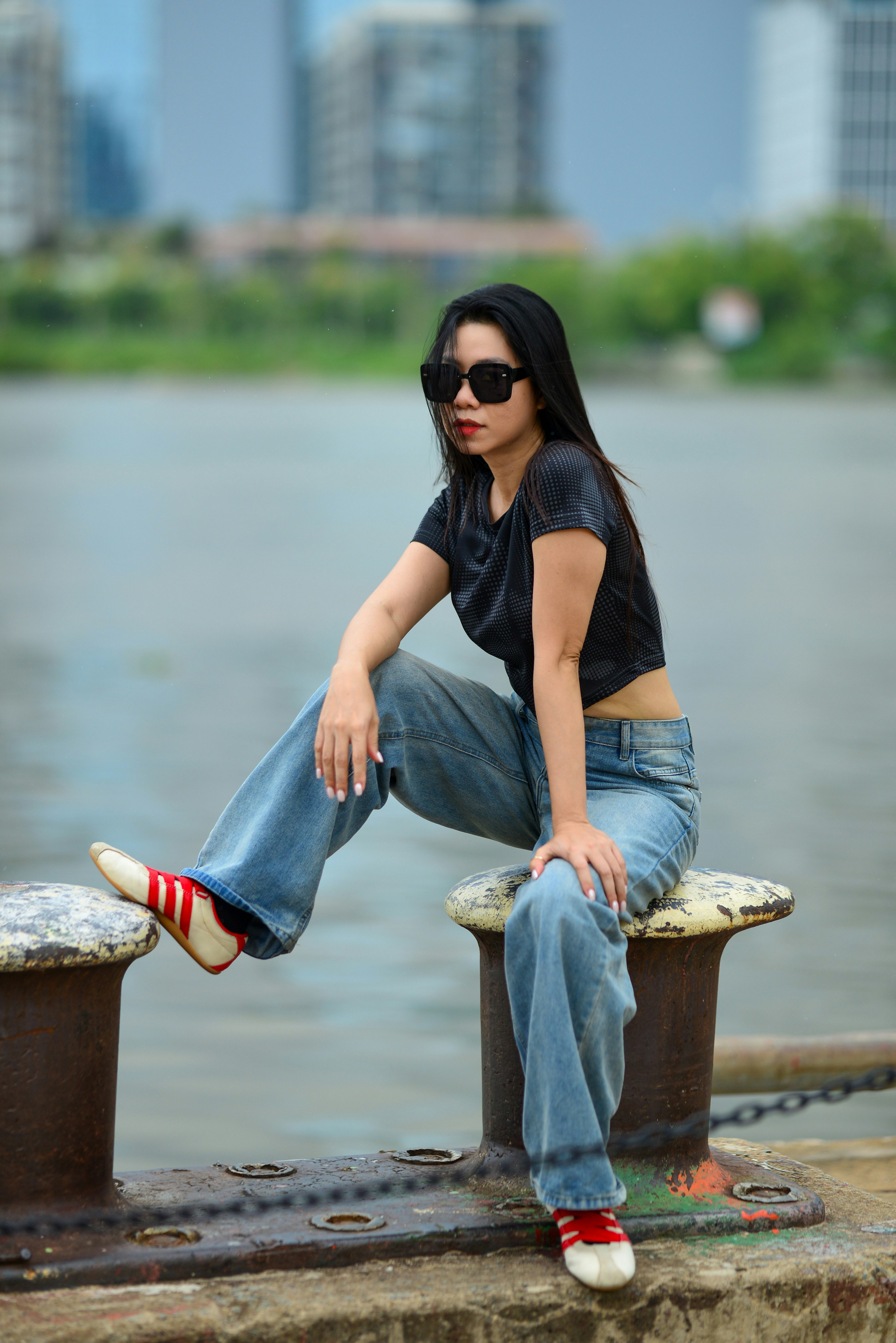 A woman in sunglasses and a black top sitting on a metal bollard