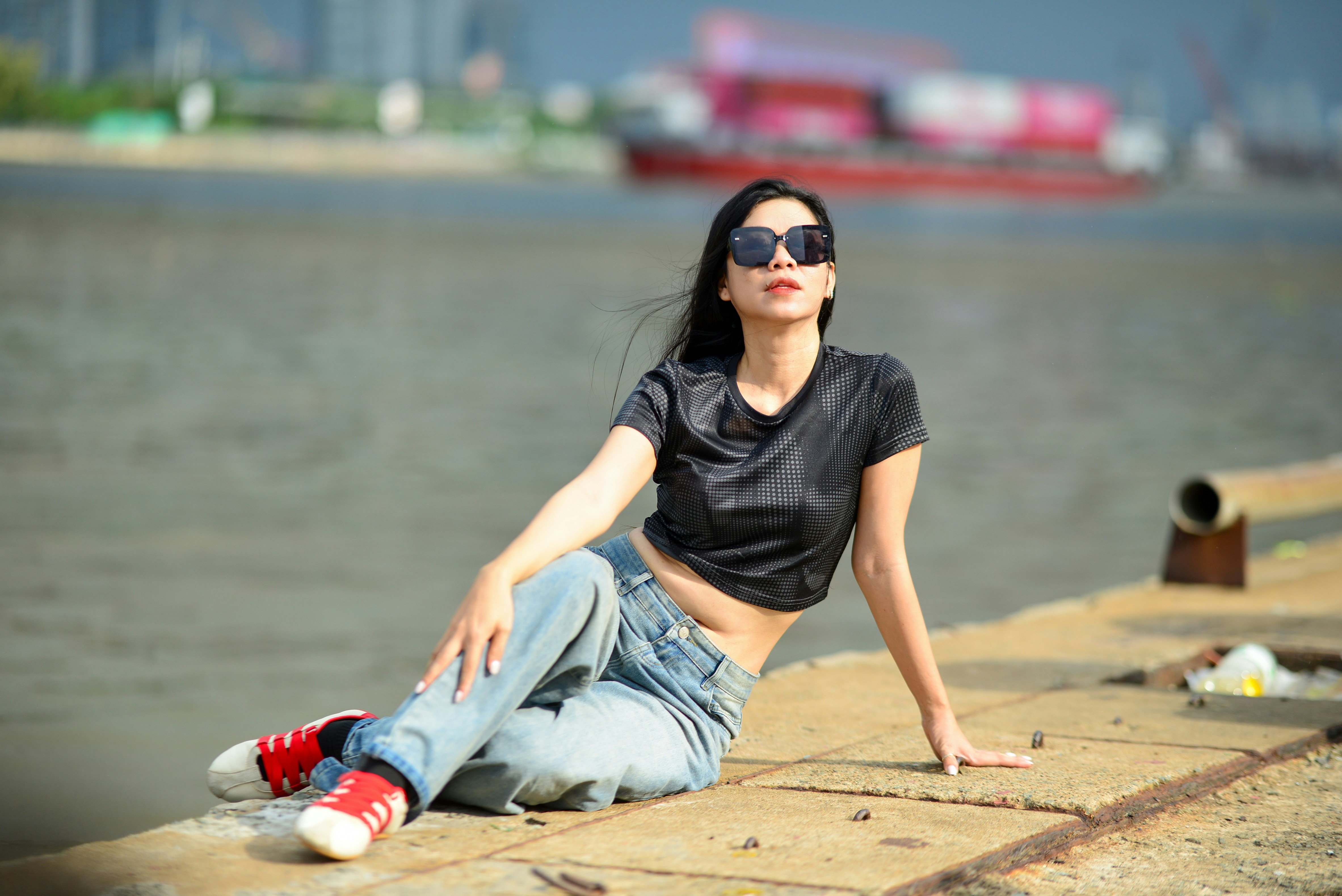 A woman in a black crop top and jeans sitting on a concrete pier