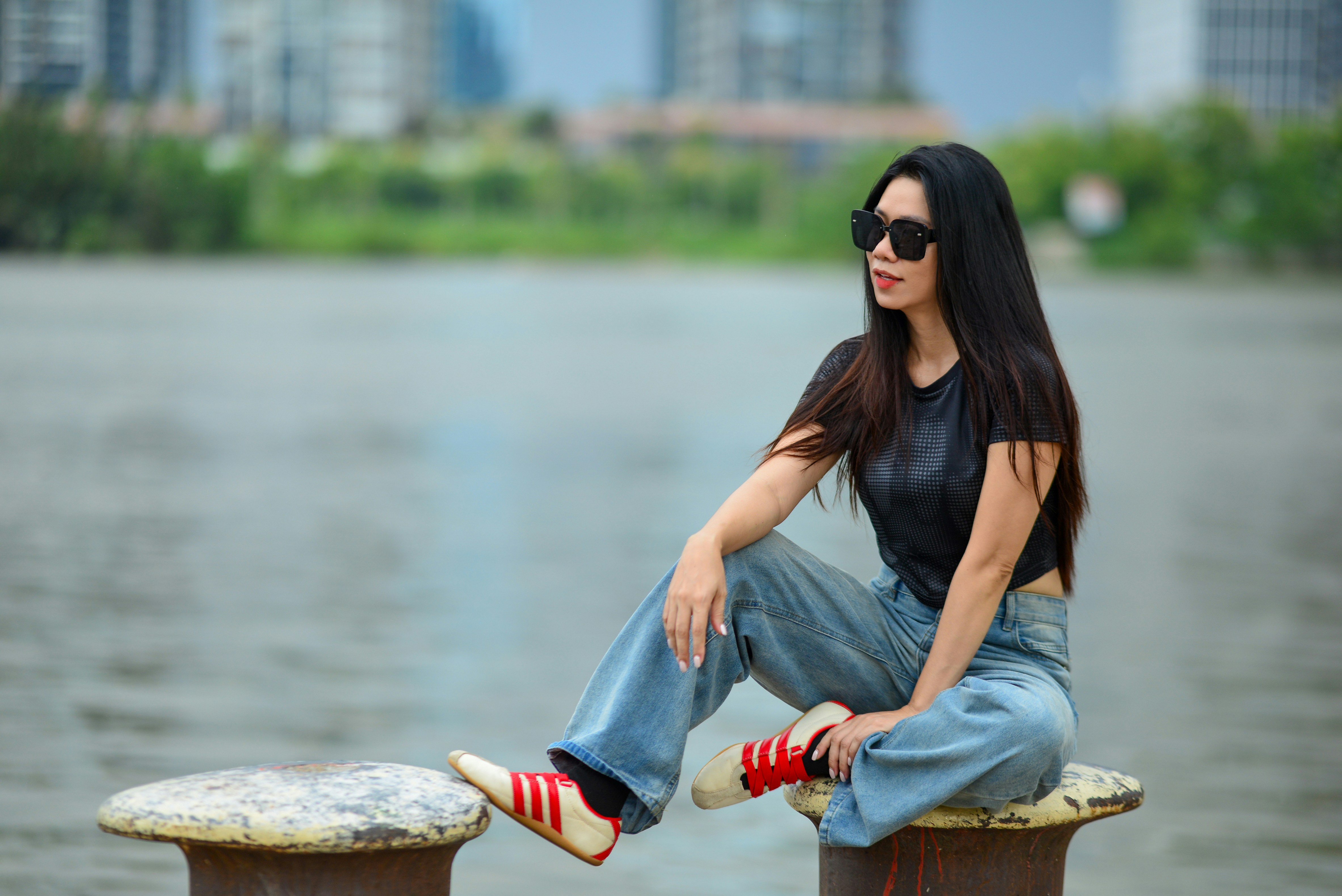 A woman in sunglasses and a black top sitting on a metal bollard