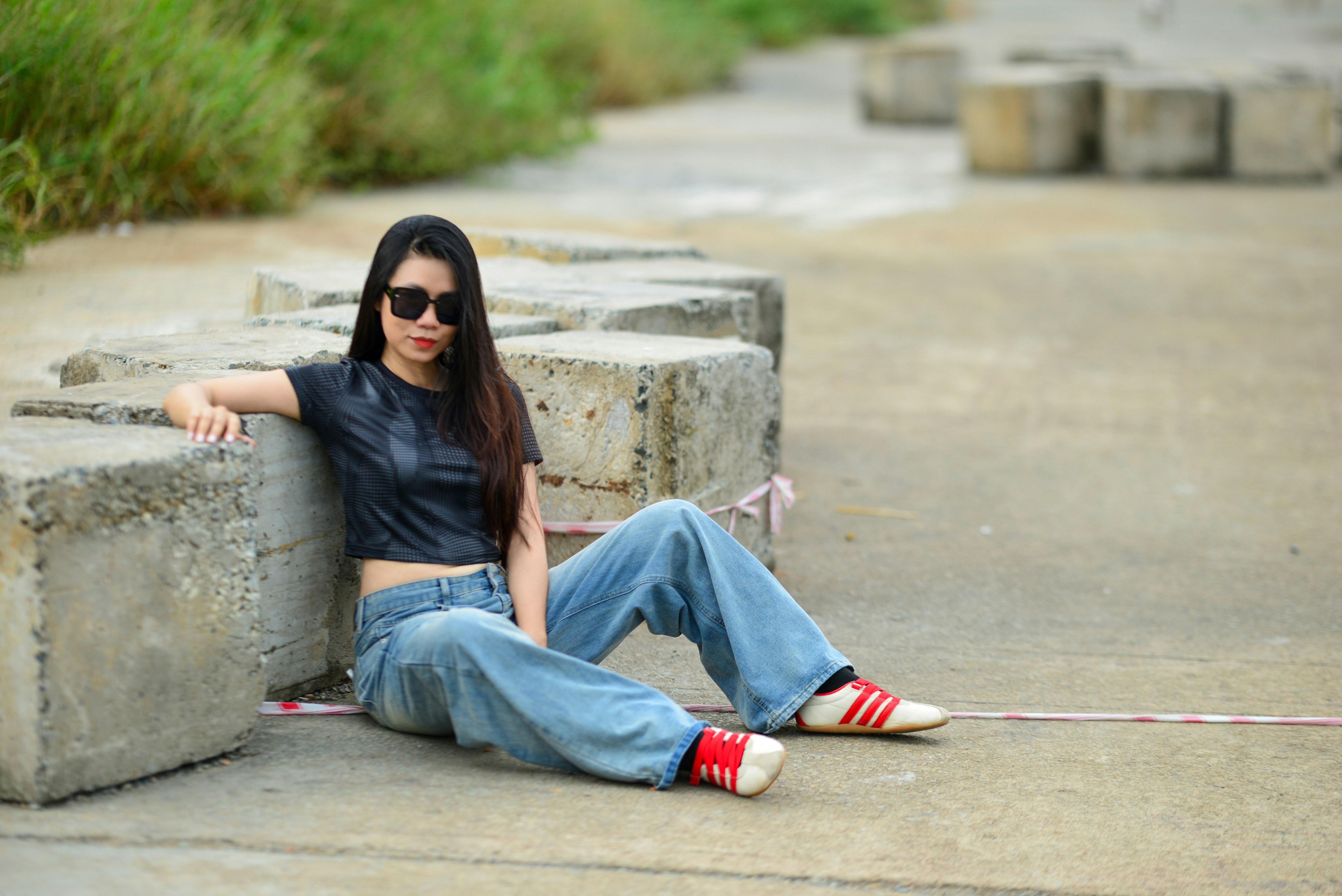 A woman in a black crop top and jeans sitting against concrete blocks