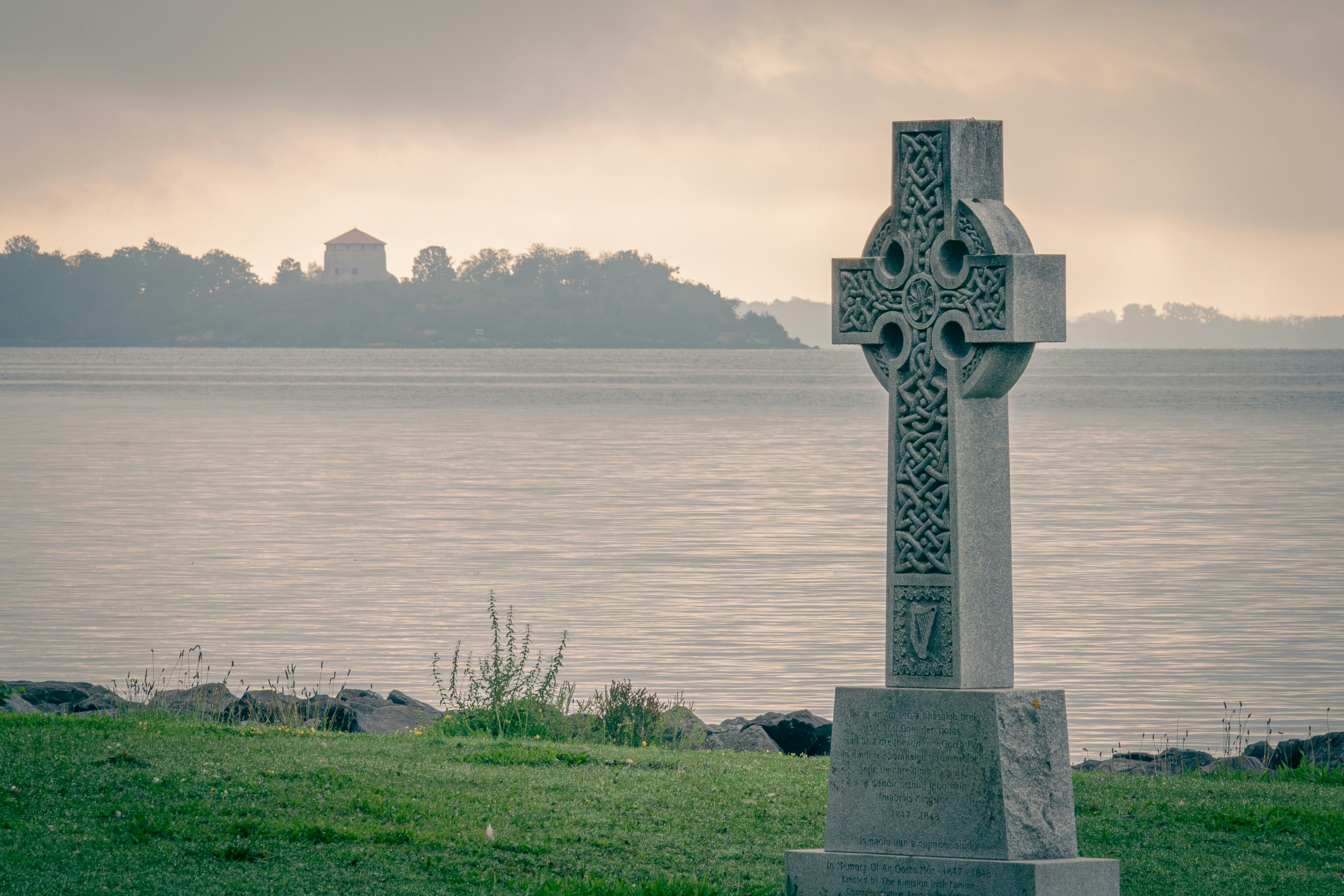 Une croix celtique de pierre sur une rive herbeuse surplombant une baie calme