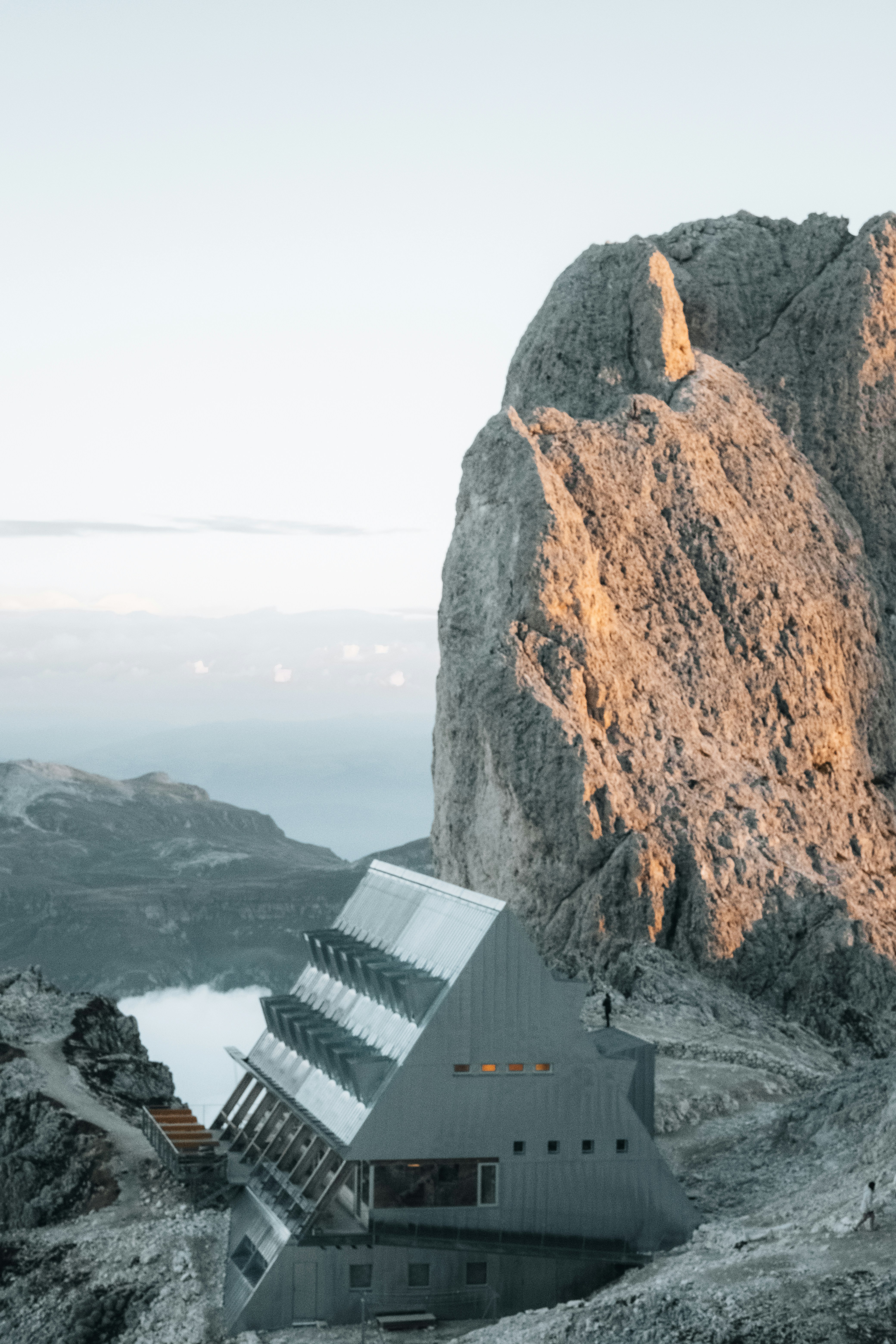 Uma cabana moderna de montanha aninhada contra uma enorme face rochosa irregular em alta altitude