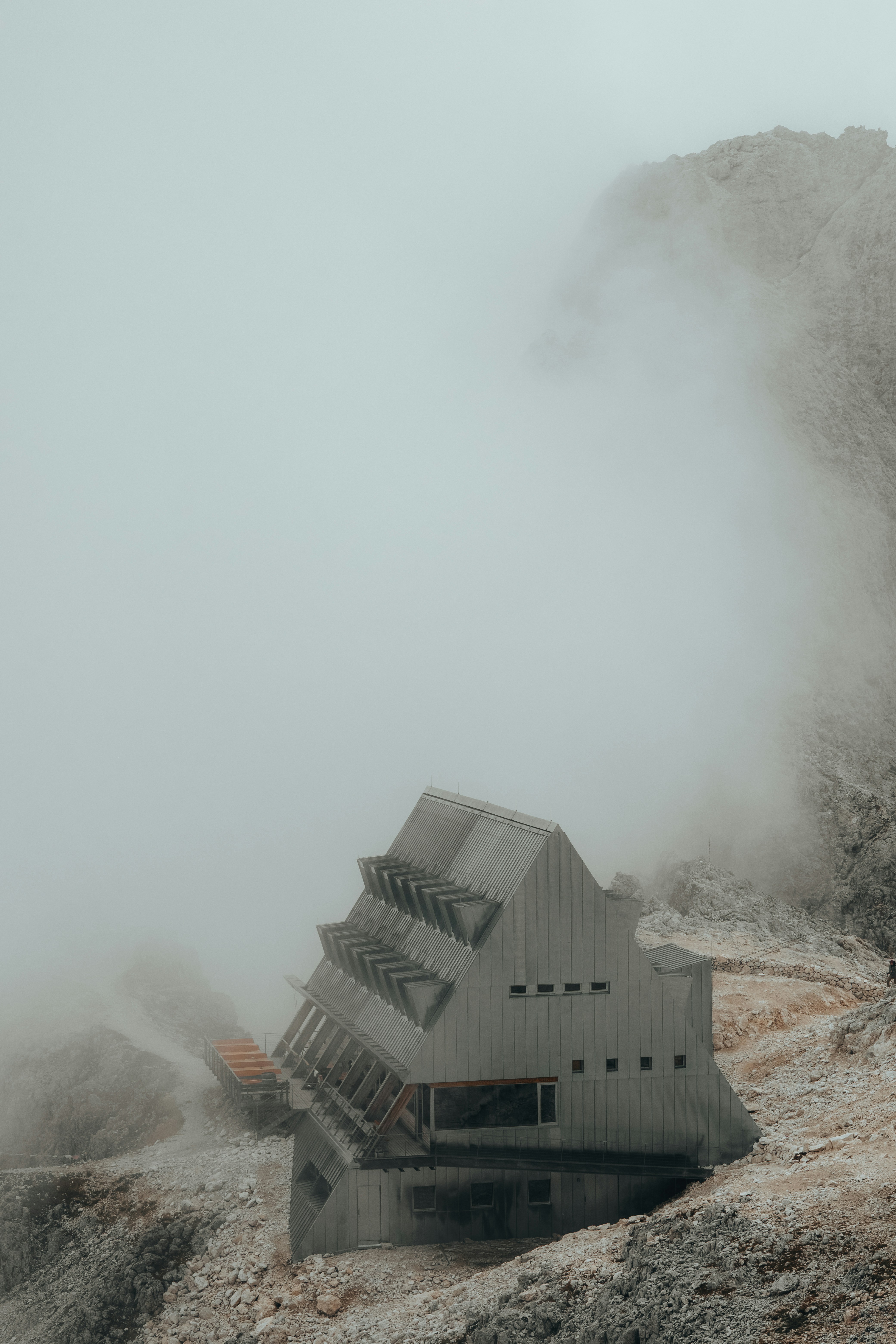 A modern metal mountain hut nestled on a rocky slope amidst thick fog