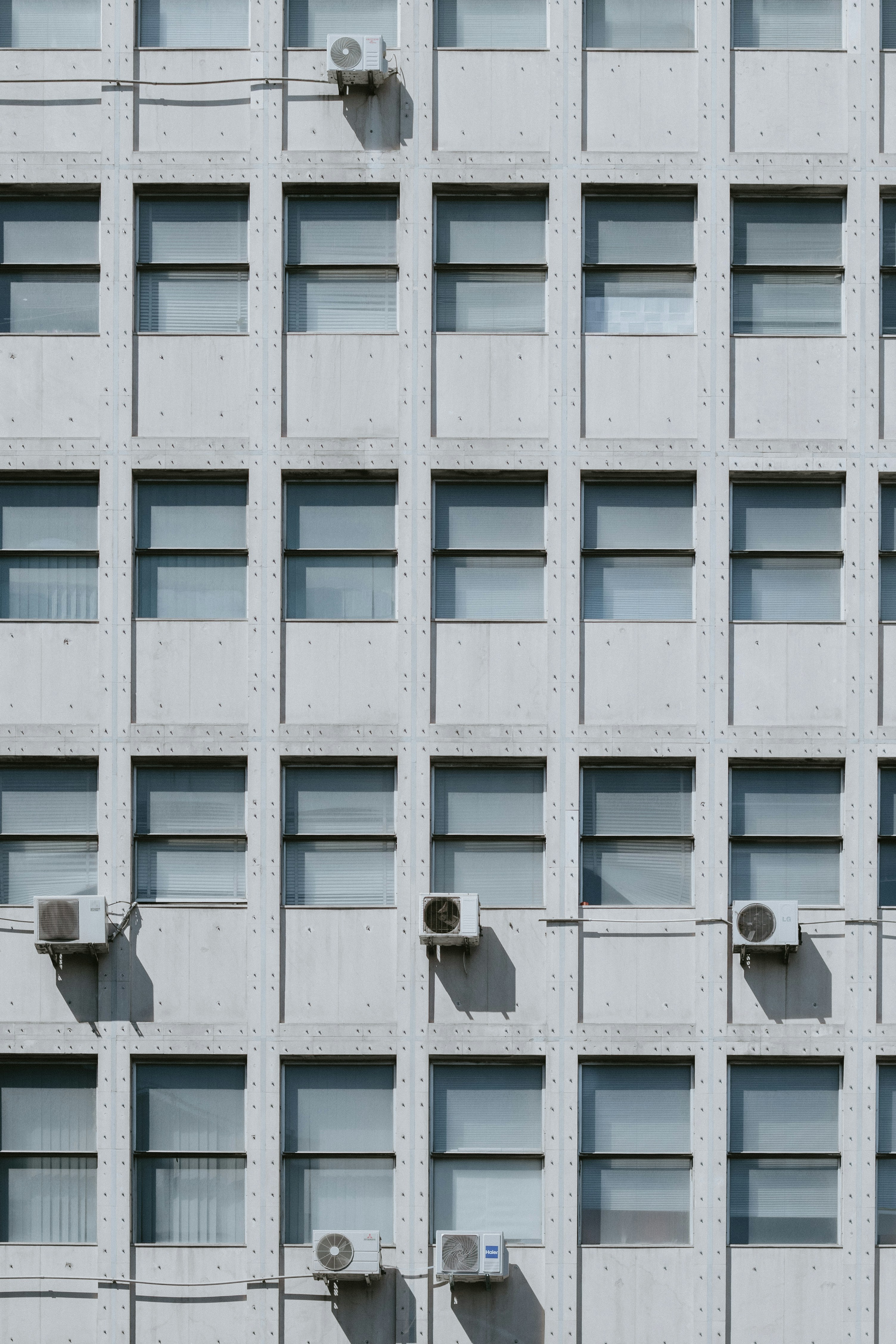 A grid of windows on a concrete building facade with several air conditioning units