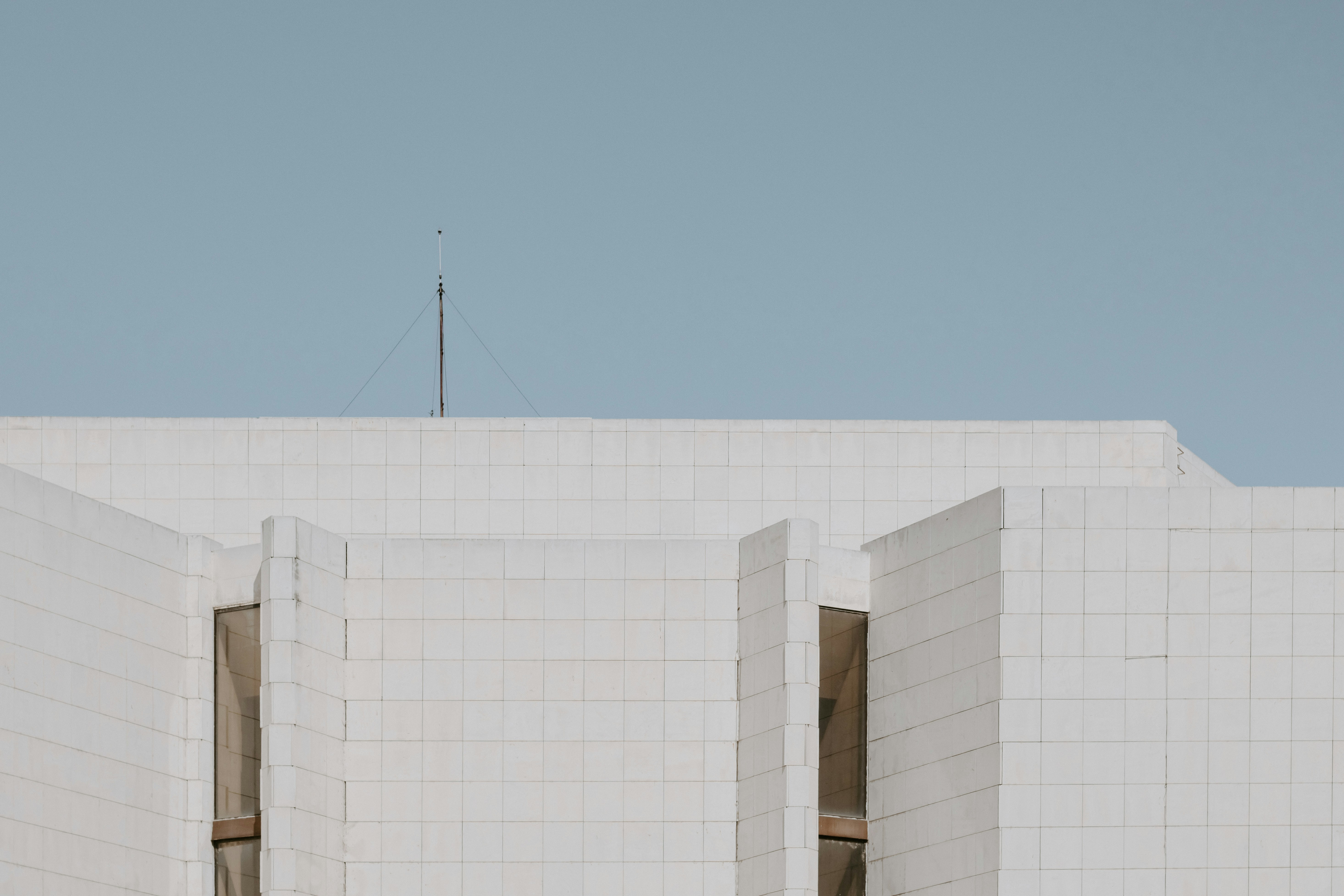 A white tiled building facade with vertical windows against a clear blue sky