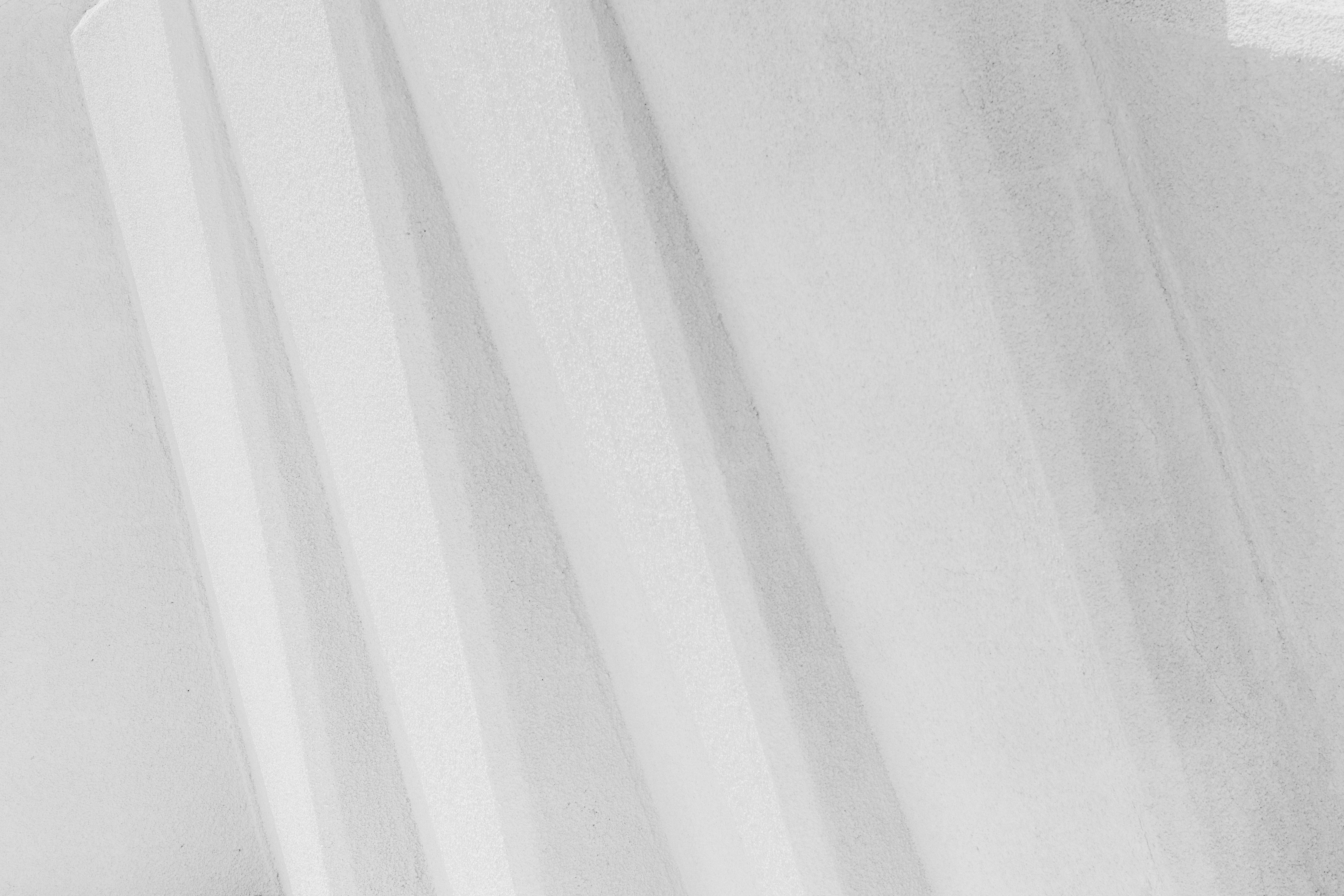 Diagonal shadows cast across a smooth white concrete wall