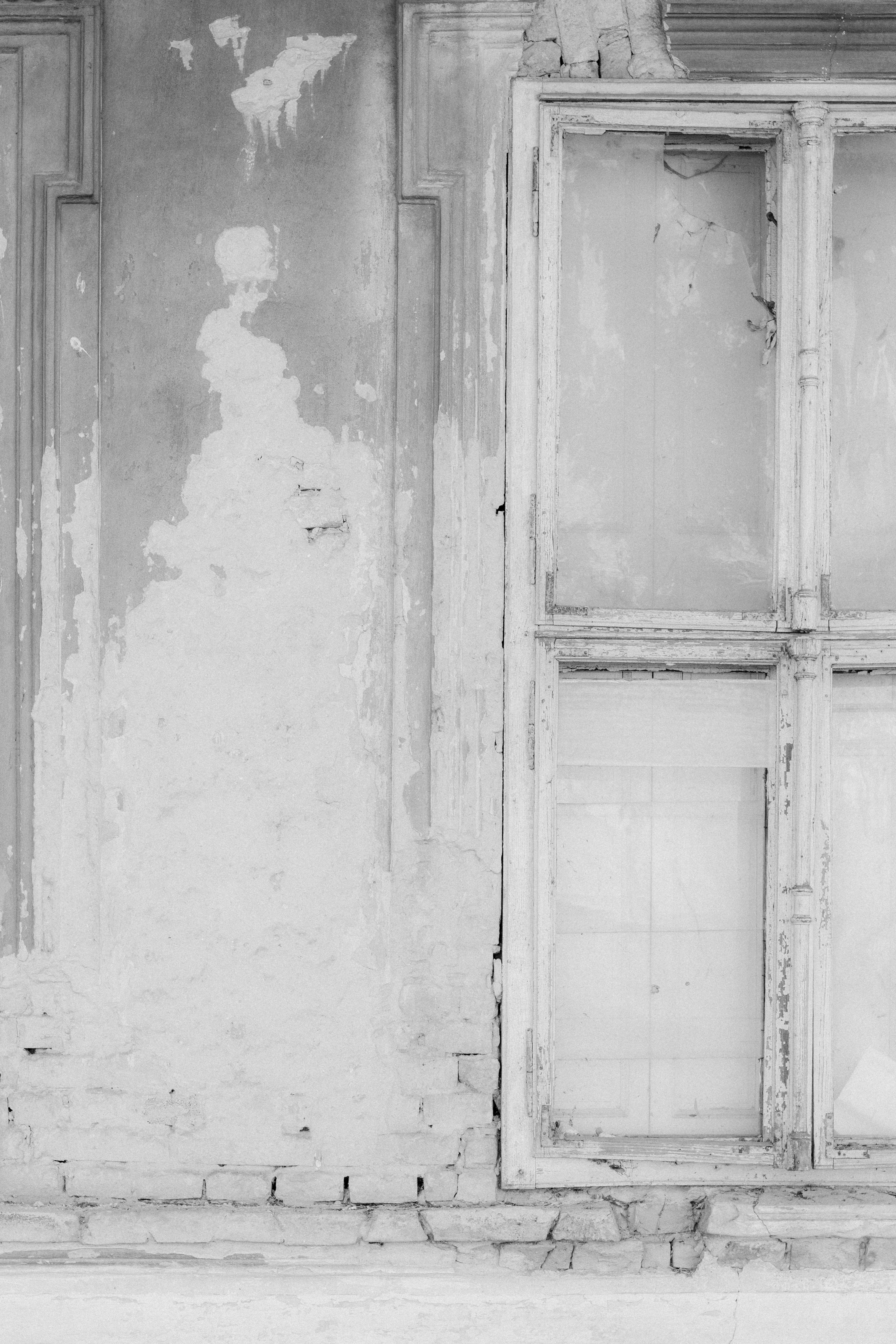A weathered wall with peeling plaster beside a tall, multi-paned wooden window